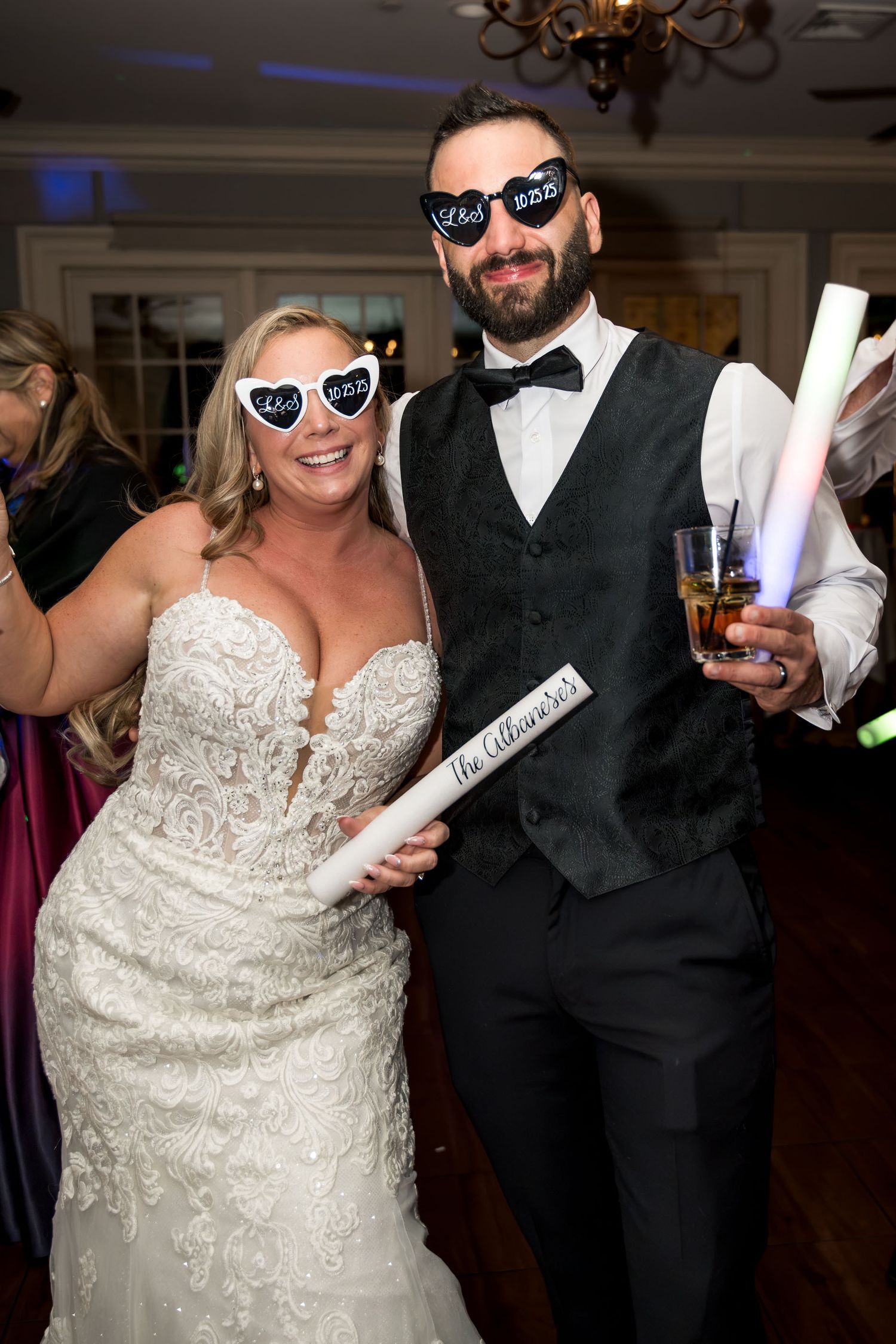 Dunes West Golf and River CBride and groom posing at reception wearing novelty heart-shaped sunglasses while holding glow sticks and drinks.