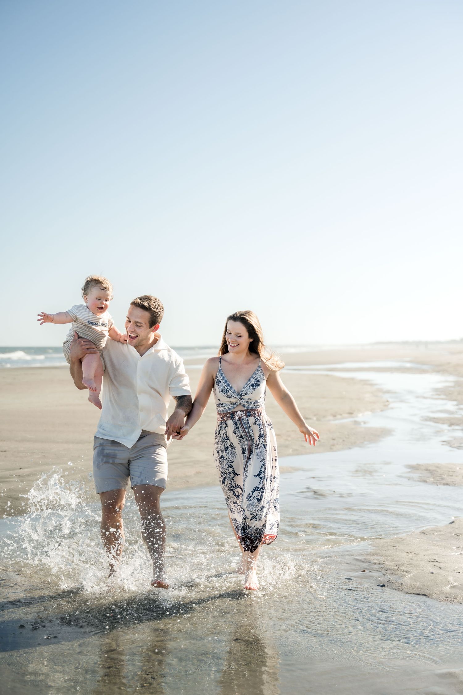 Isle of Palms. Happy young family splashing through ocean waves on a sunny beach, parents holding their toddler.