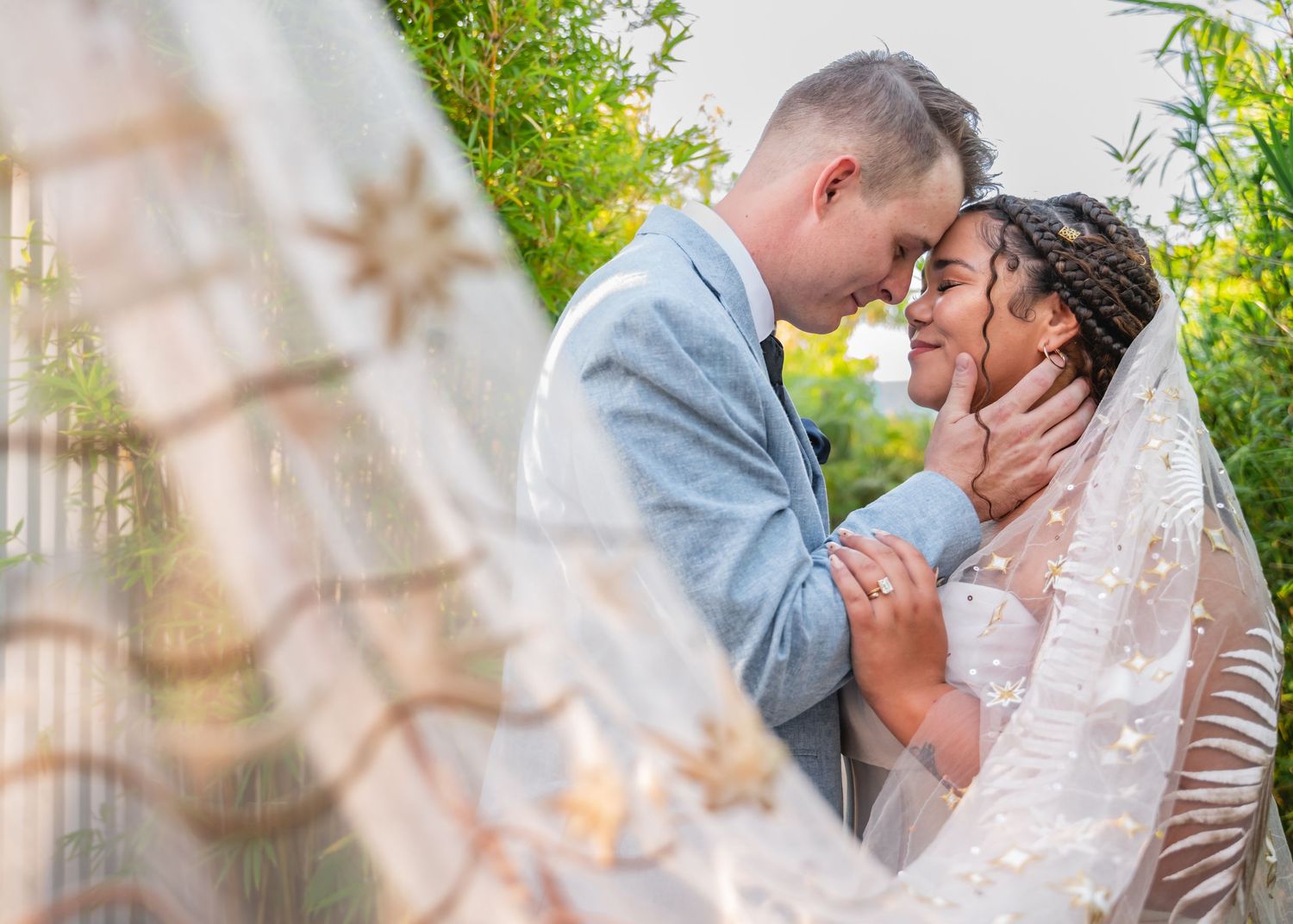 A romantic wedding couple shares tender kisses in a garden setting with lush greenery and natural lighting.