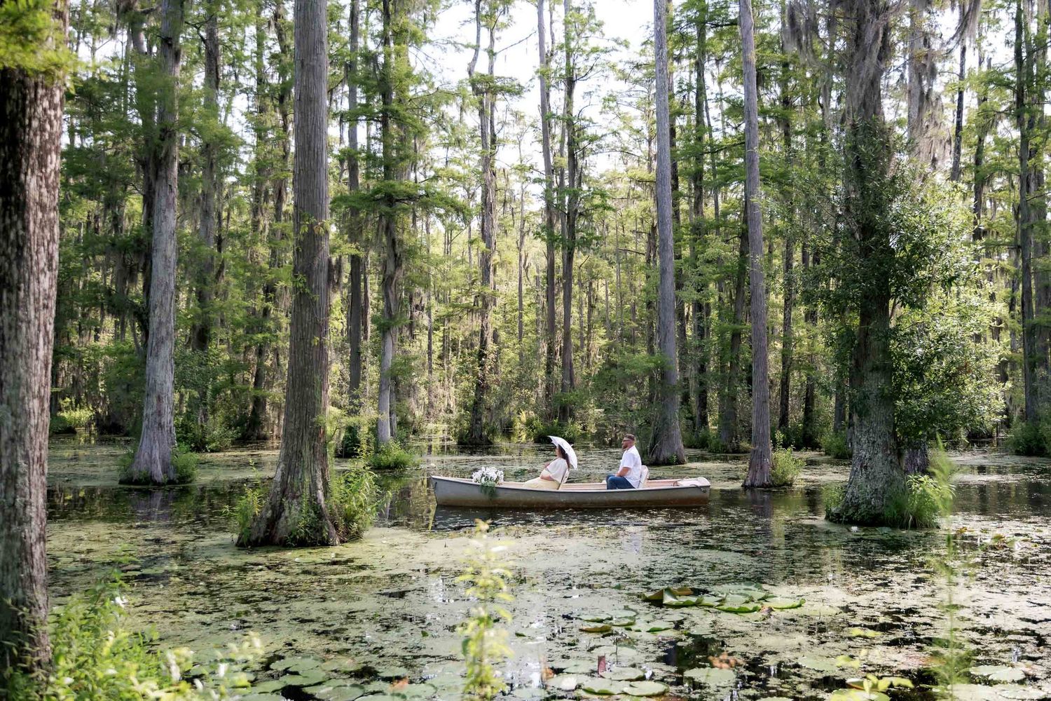 Two people canoeing through a serene cypress swamp with lily pads and moss-draped trees.