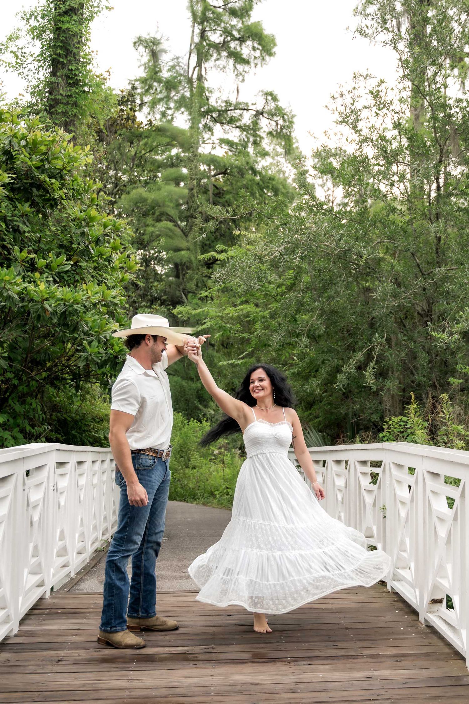 Cypress Gardens. Couple dancing on a white wooden bridge surrounded by lush green trees outdoors.