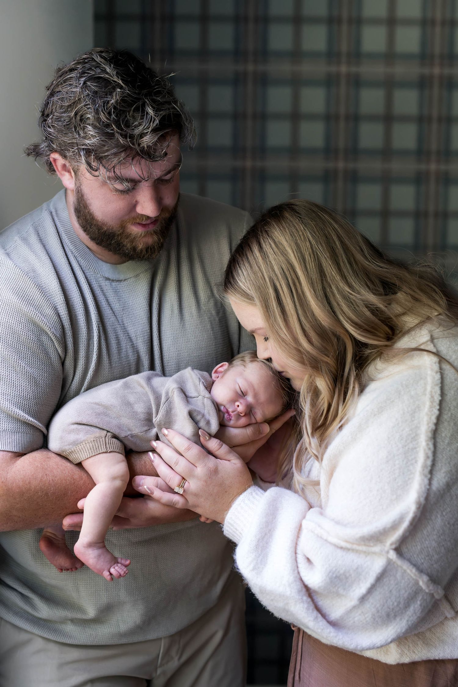 New parents lovingly gaze at their newborn baby, with dad in gray and mom in white sweater.