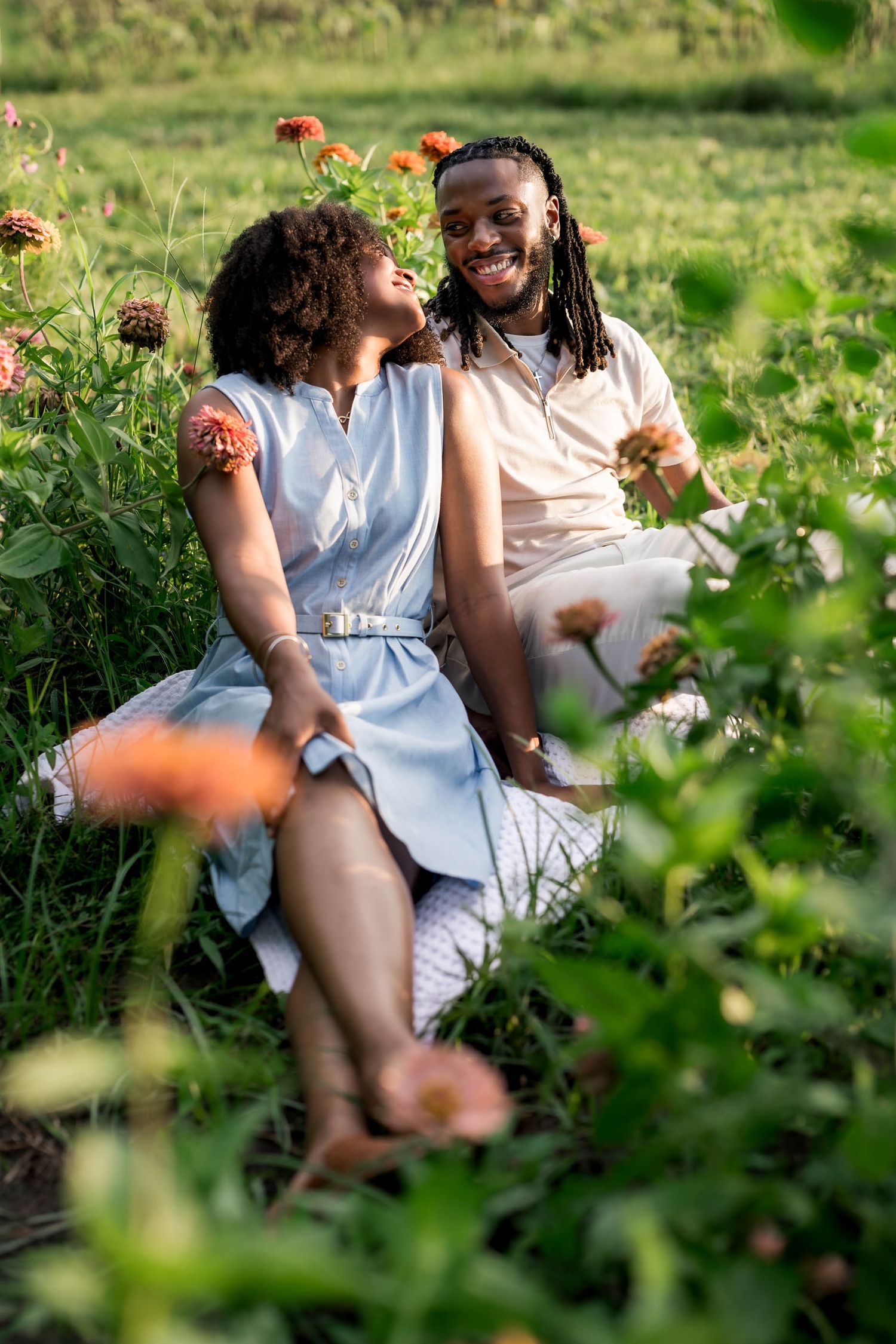 A happy couple sits together in a lush flower field, smiling and enjoying a romantic outdoor moment.