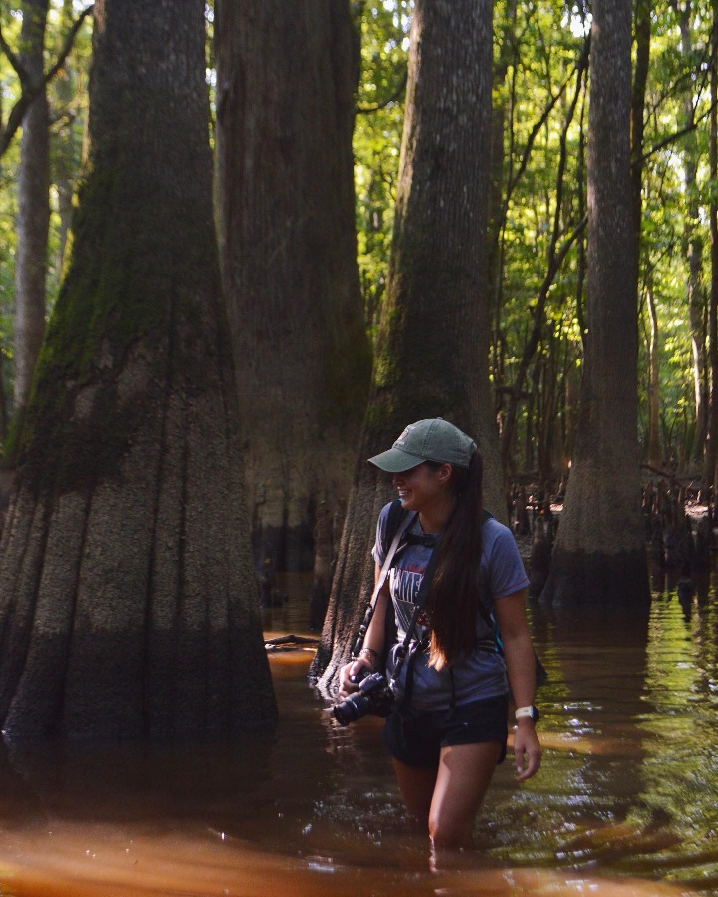 Female photographer wading through shallow water in a cypress forest while holding her camera.