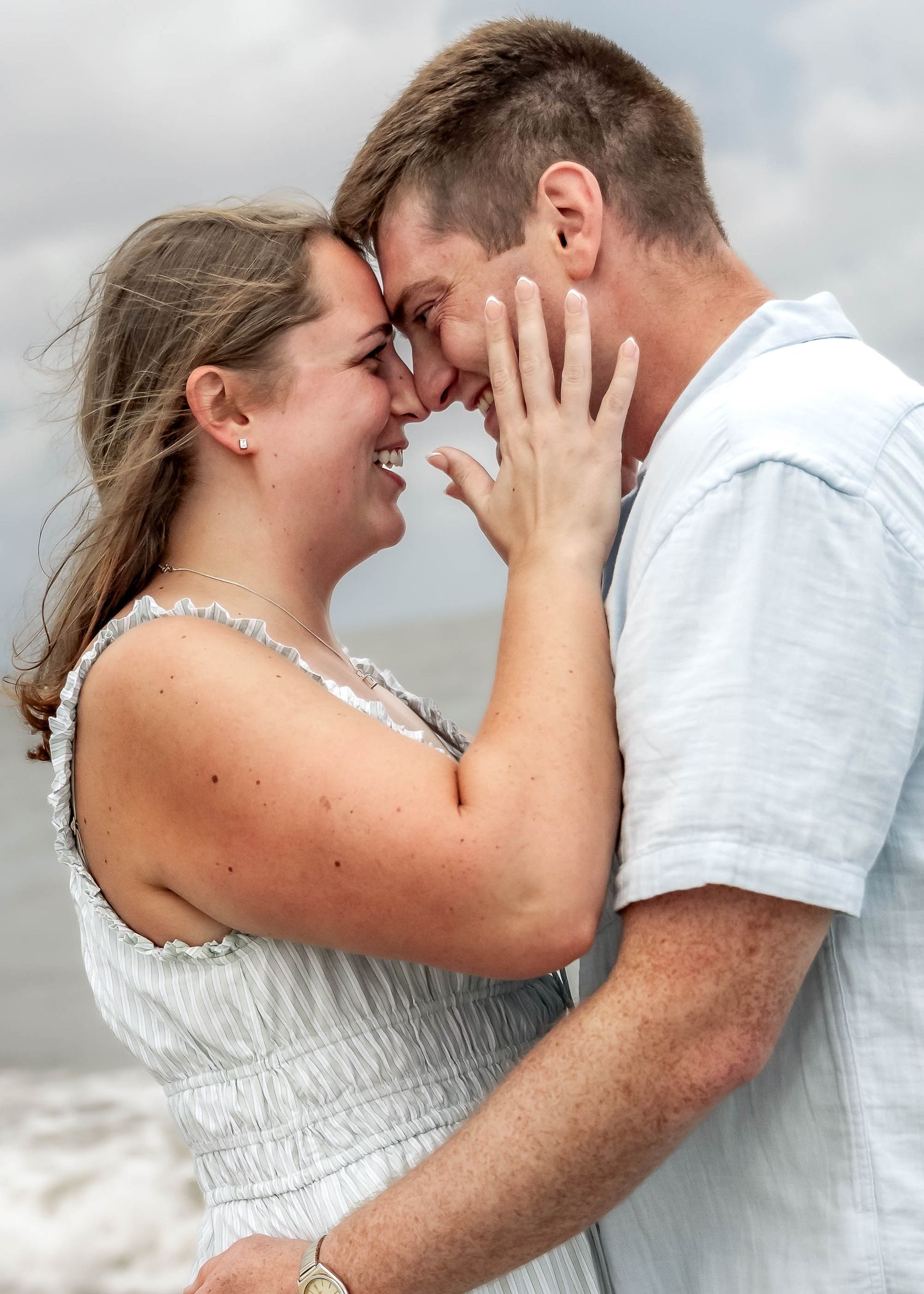 Folly Beach. Joyful couple touching foreheads and smiling at beach, woman showing engagement ring to camera.