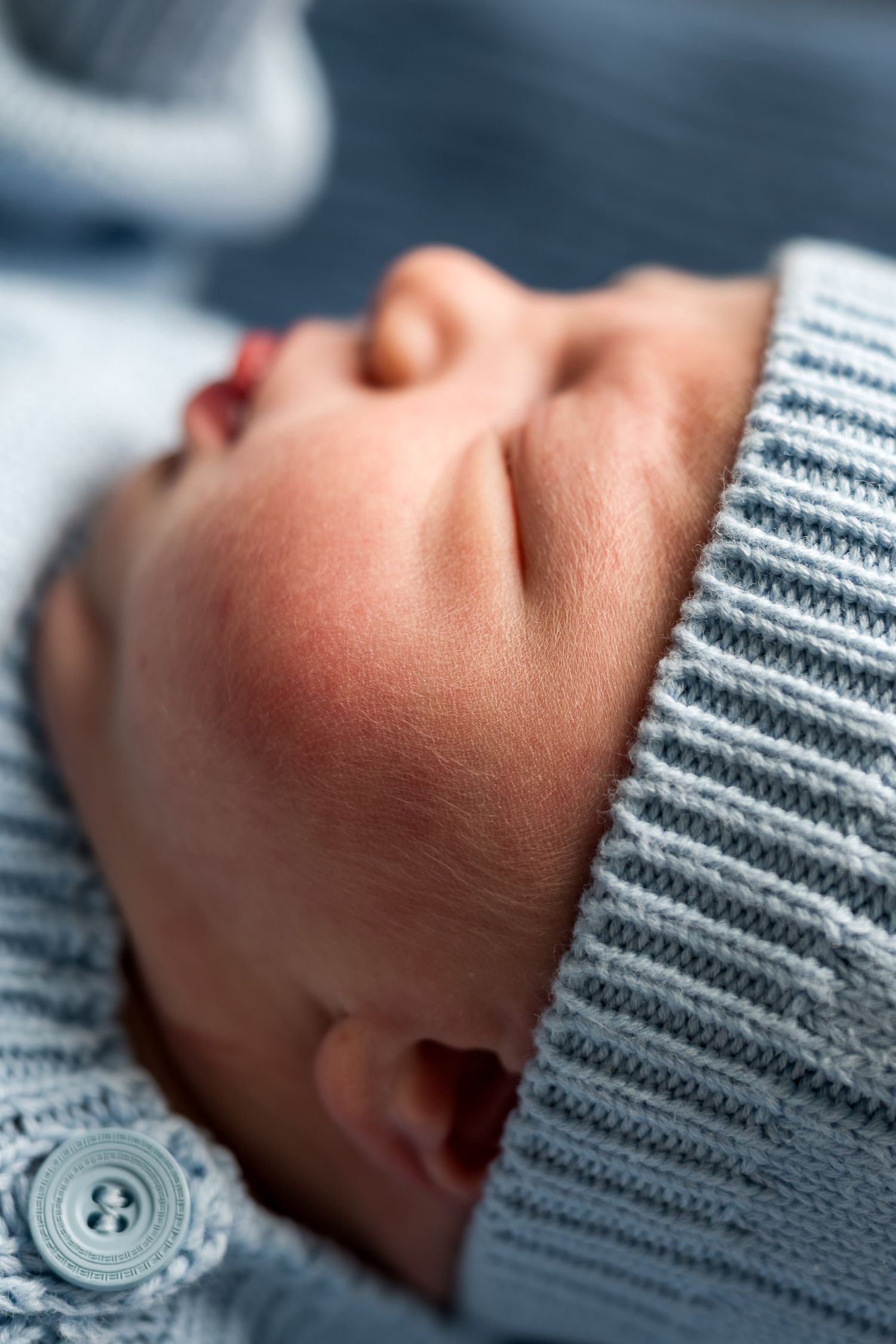 Close-up portrait of a sleeping newborn baby wearing a soft blue knit hat and matching outfit.