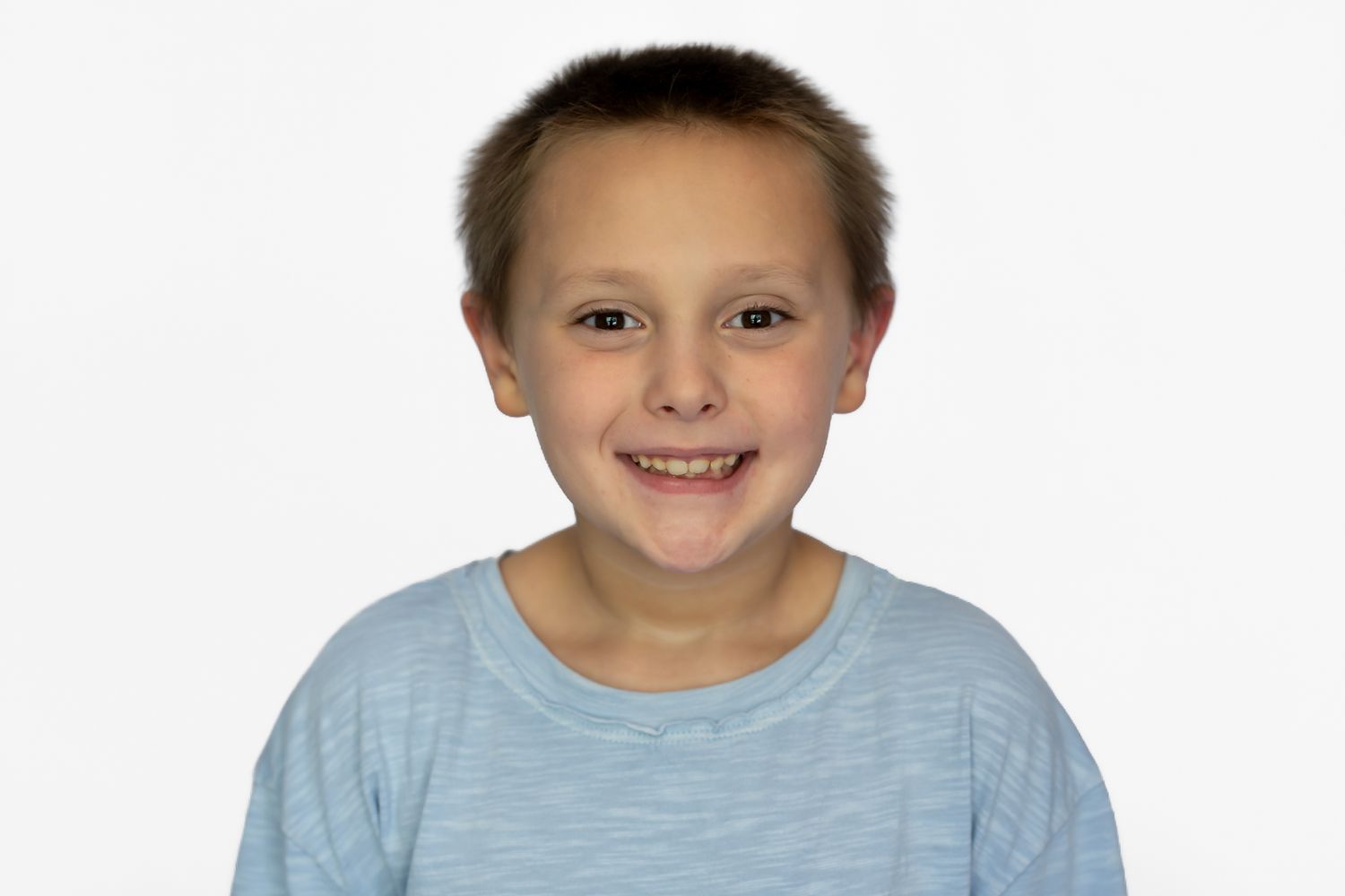 Smiling young boy with short brown hair wearing a light blue t-shirt against a white background.