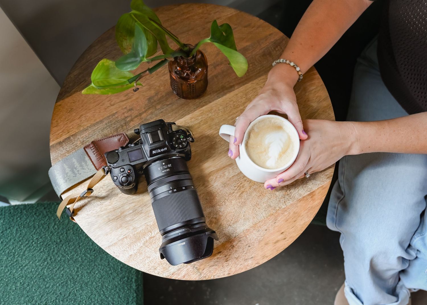 Overhead view of a photographer holding a latte beside a professional camera on a wooden table.