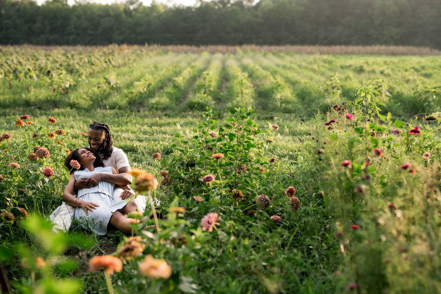 Couple sitting together in a lush flower field with pink blooms at golden hour.
