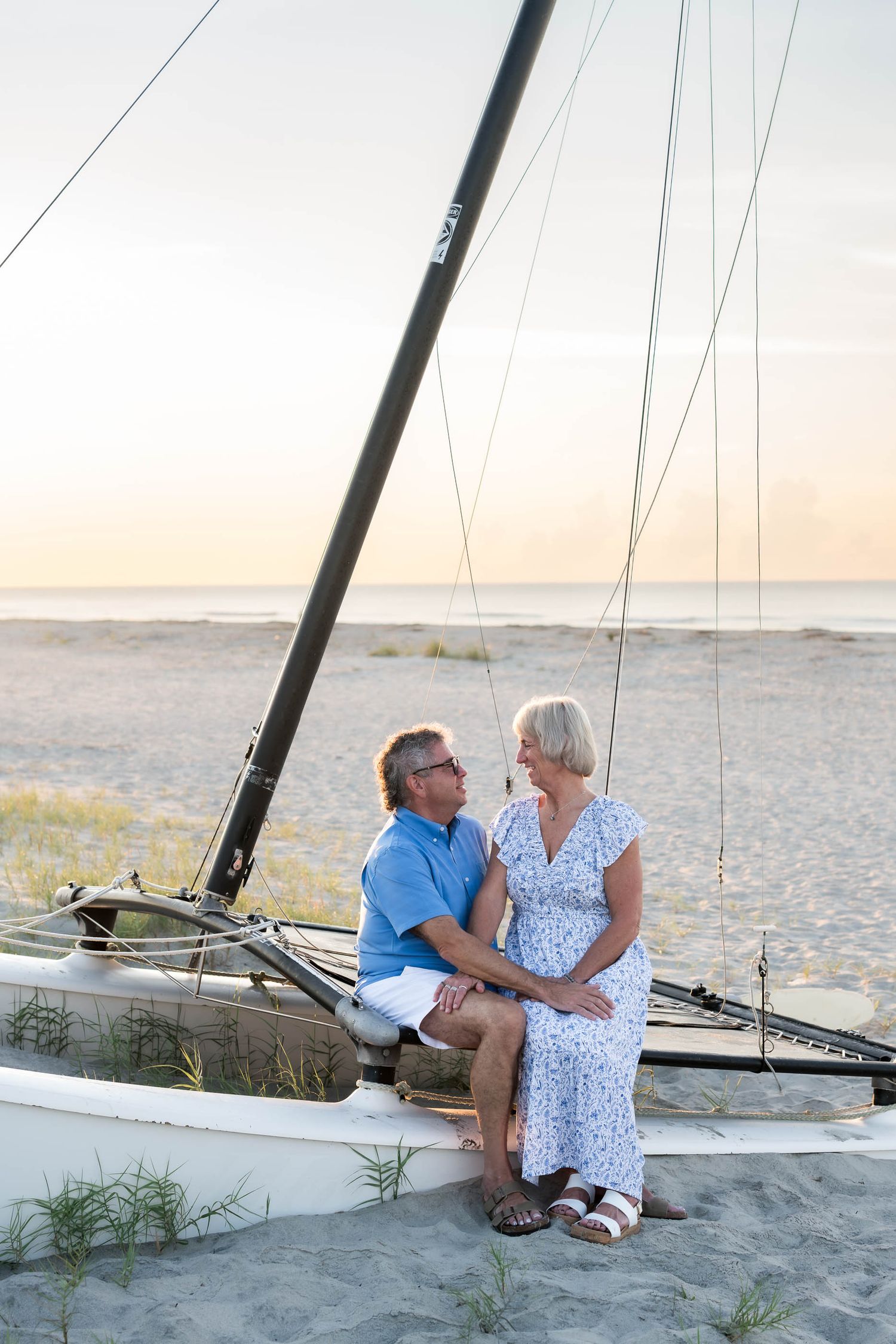 Mature couple sitting together on a catamaran hull on the beach at golden hour.