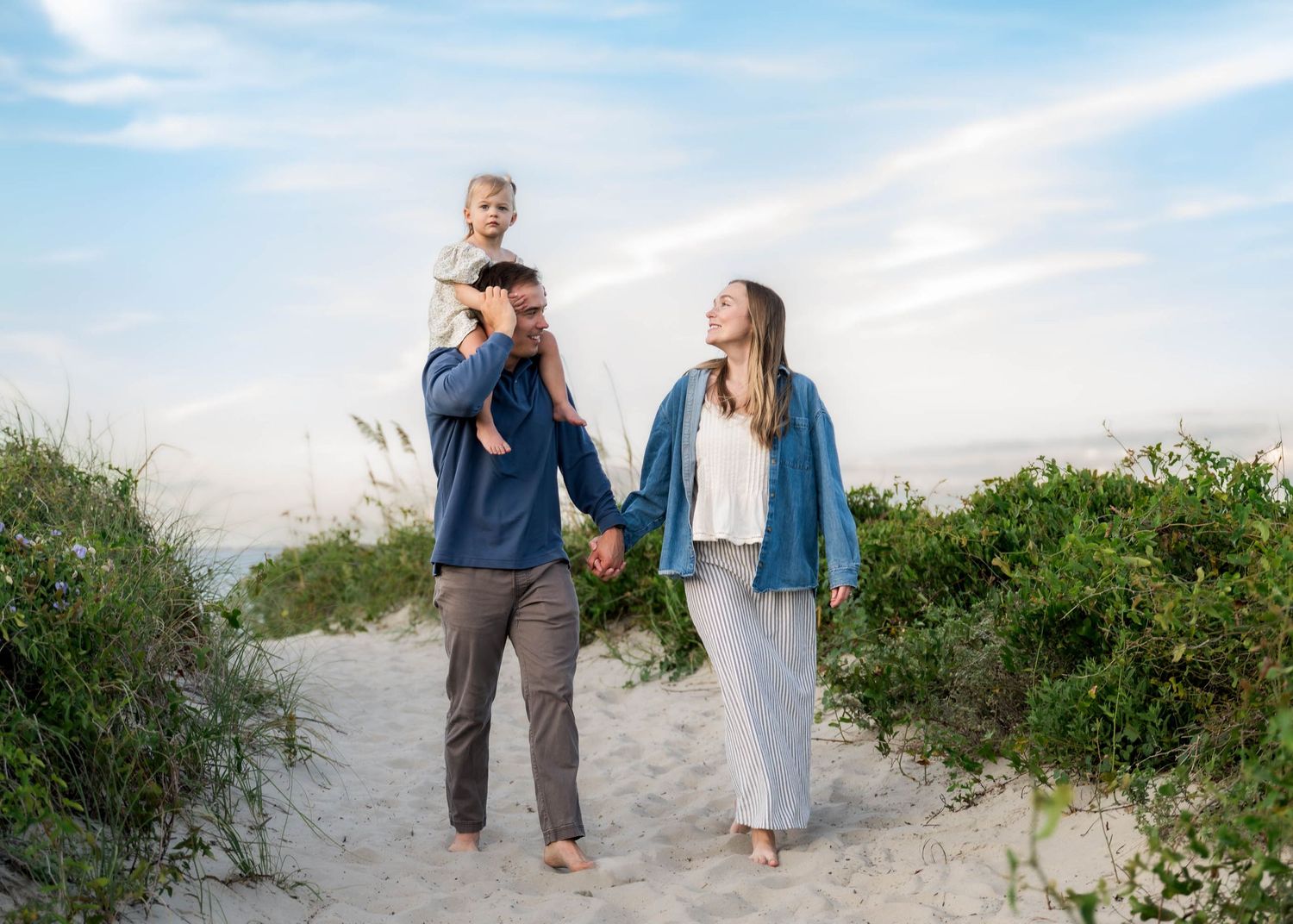 Folly Beach. Happy family with toddler on dad's shoulders walking on sandy beach path at sunset.