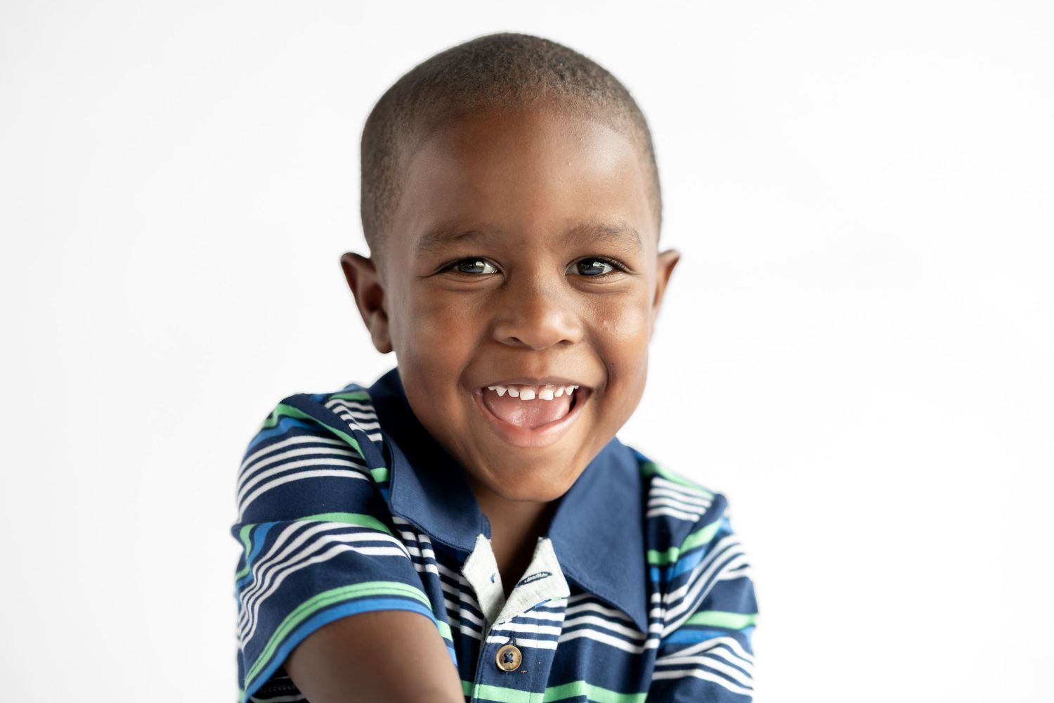 Smiling young Black boy in striped polo shirt posing cheerfully against white background.