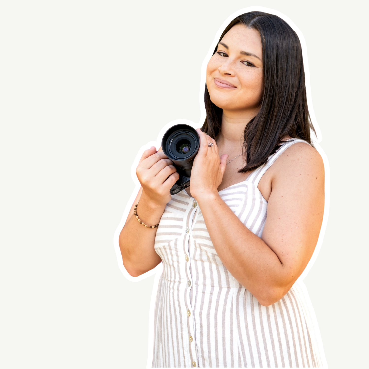 Smiling woman in striped dress holding a camera lens, posing against a light background.