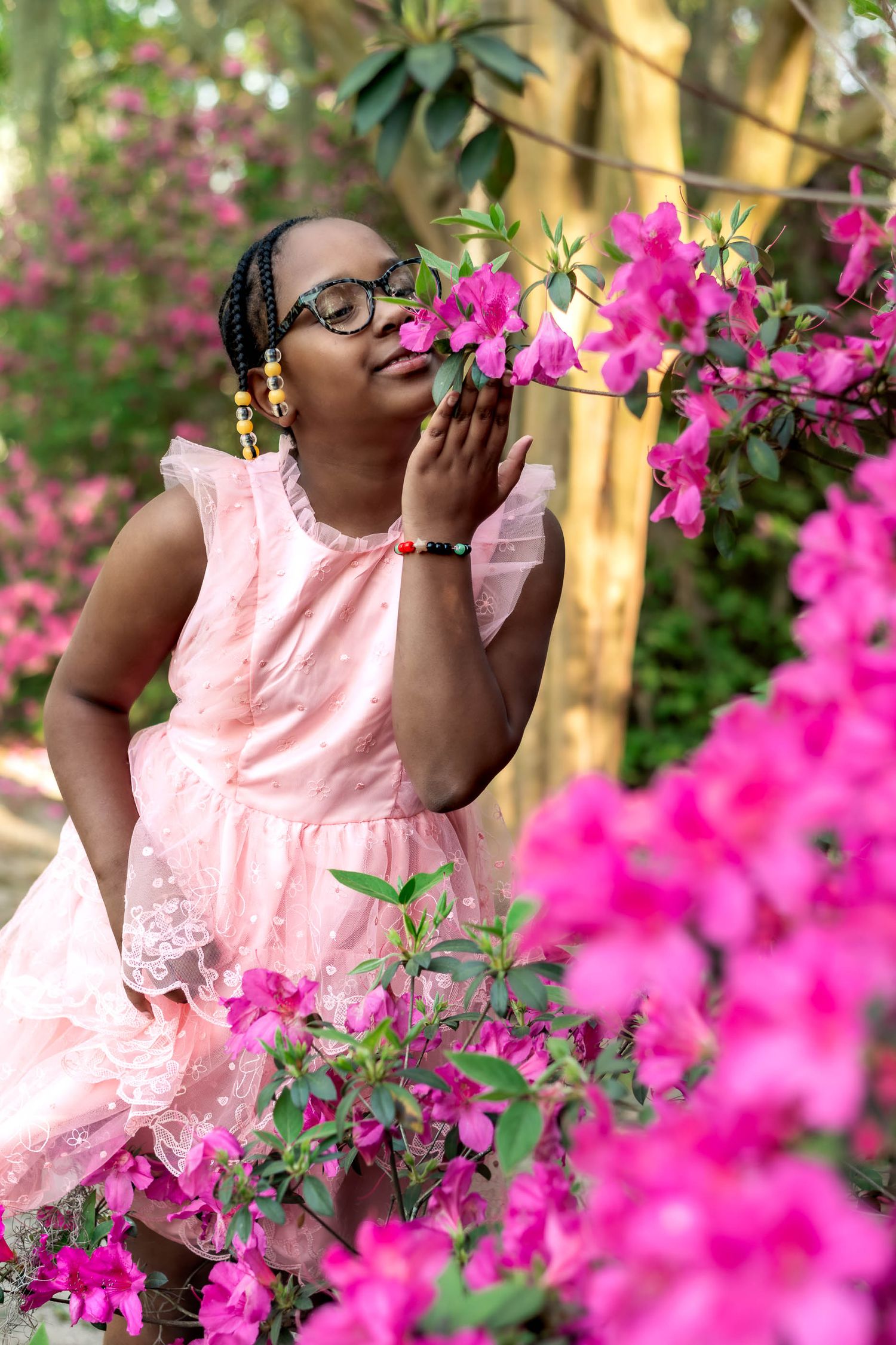 Hampton Park. Young girl in pink dress smelling vibrant pink azalea flowers in a garden.