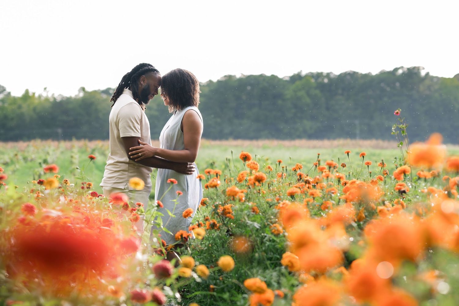 Couple embracing romantically in a vibrant field of orange and red flowers with lush green trees in the background.