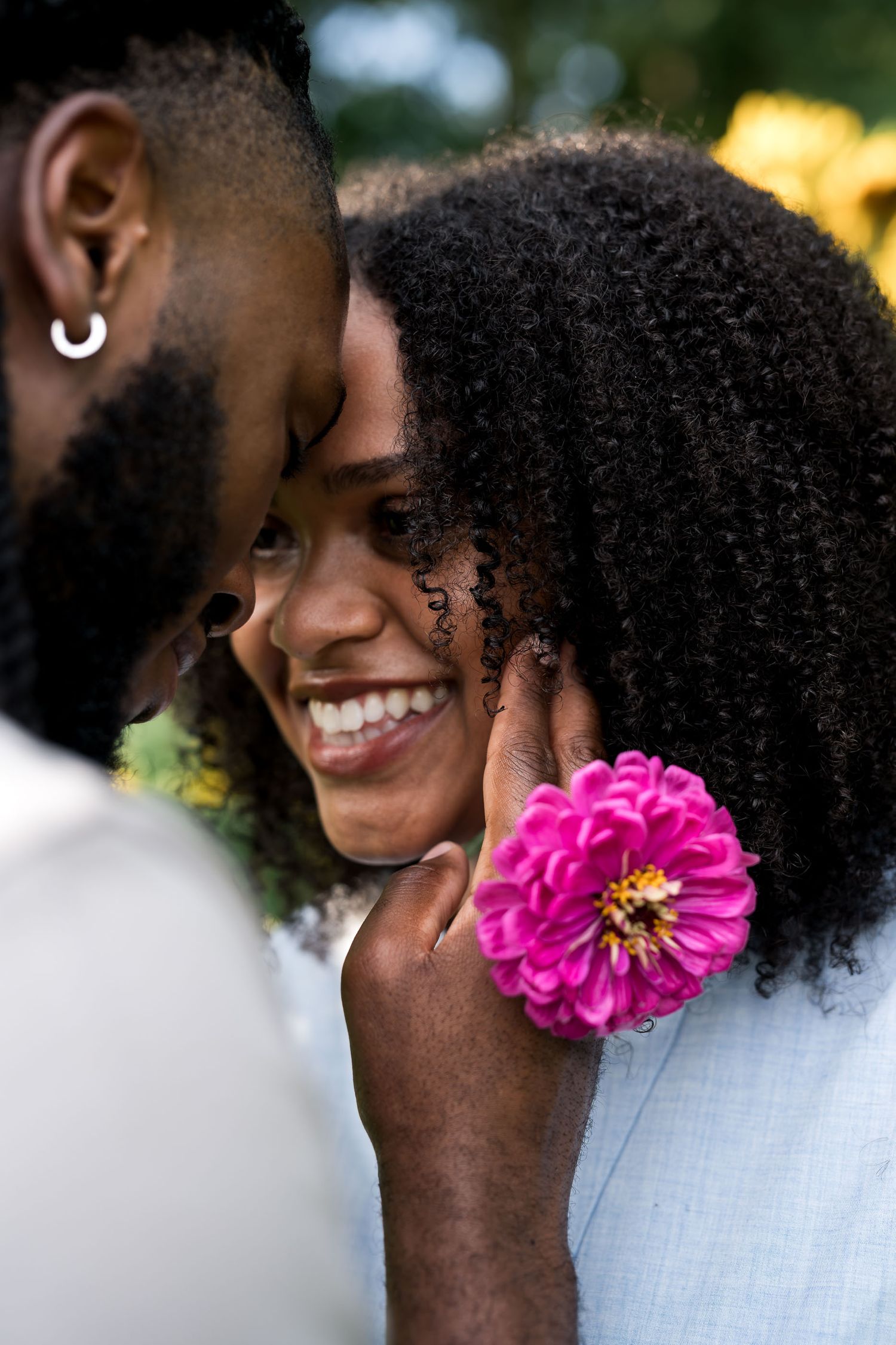 A joyful Black couple shares an intimate moment, with a man holding a pink flower against a smiling woman's cheek.