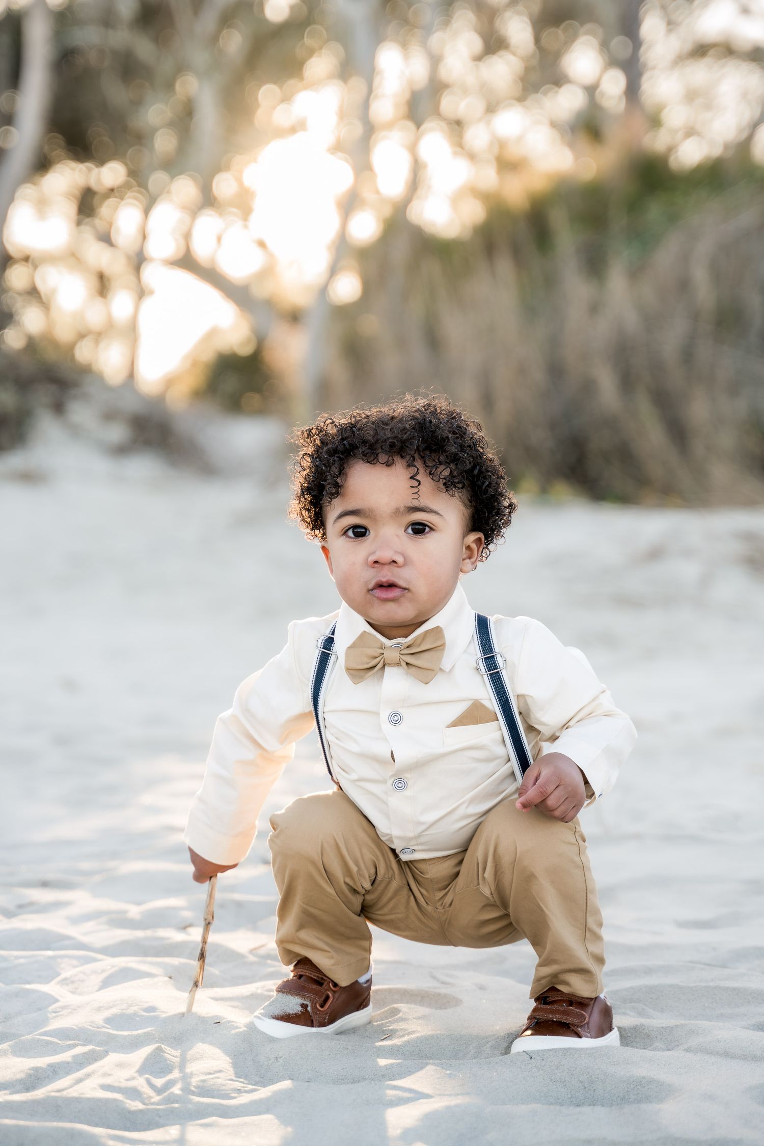 Folly Beach. Adorable toddler in bow tie and suspenders crouching on sandy beach at sunset.
