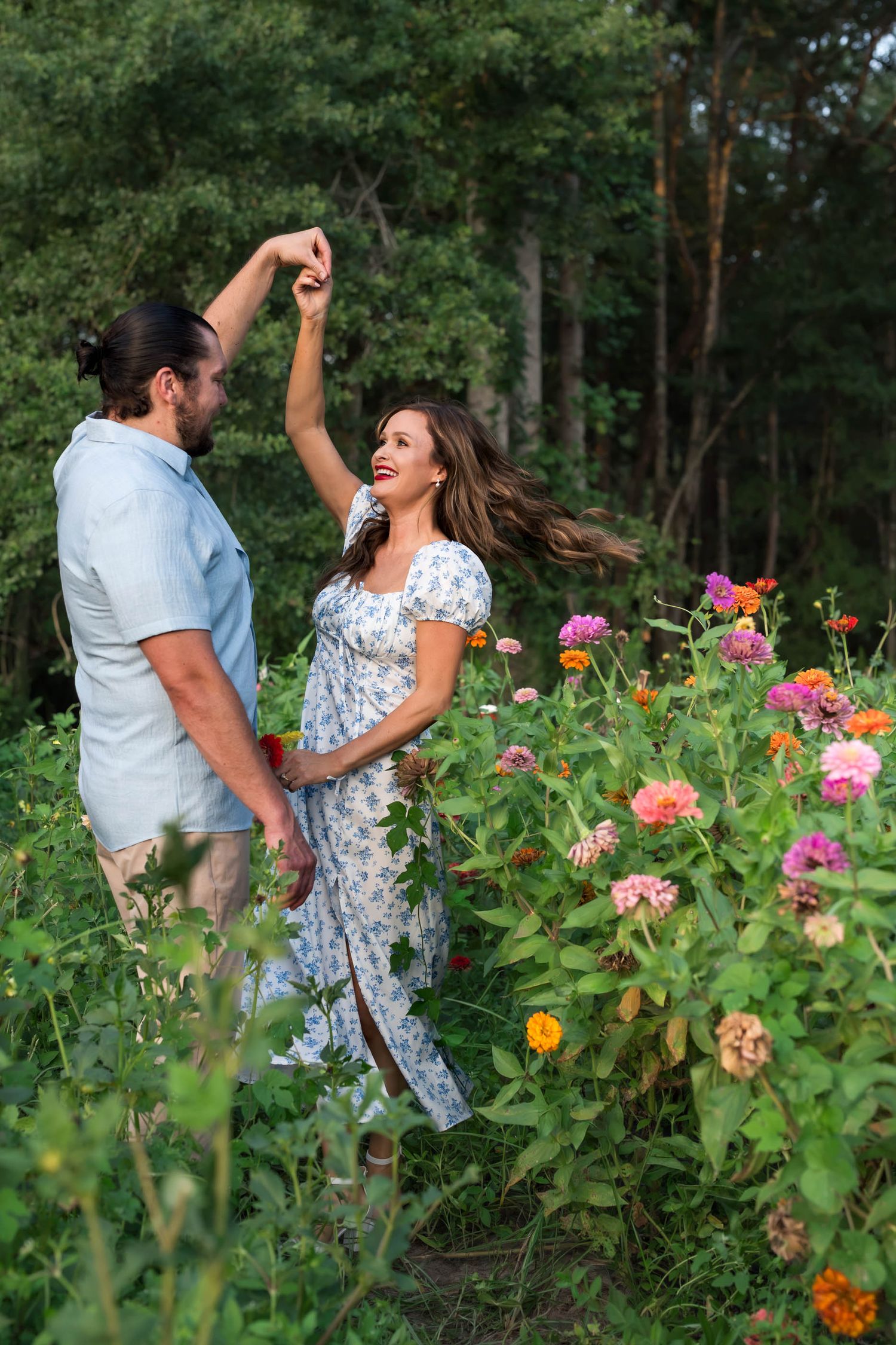 A couple dances joyfully among colorful zinnia flowers in a lush garden, the woman spinning in a floral dress.