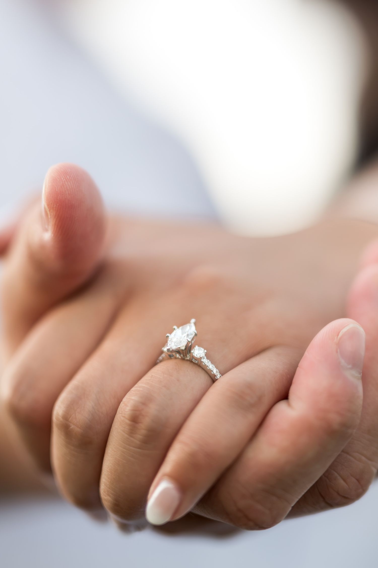 Close-up of hands holding, showcasing a stunning marquise diamond three-stone engagement ring on a silver band.