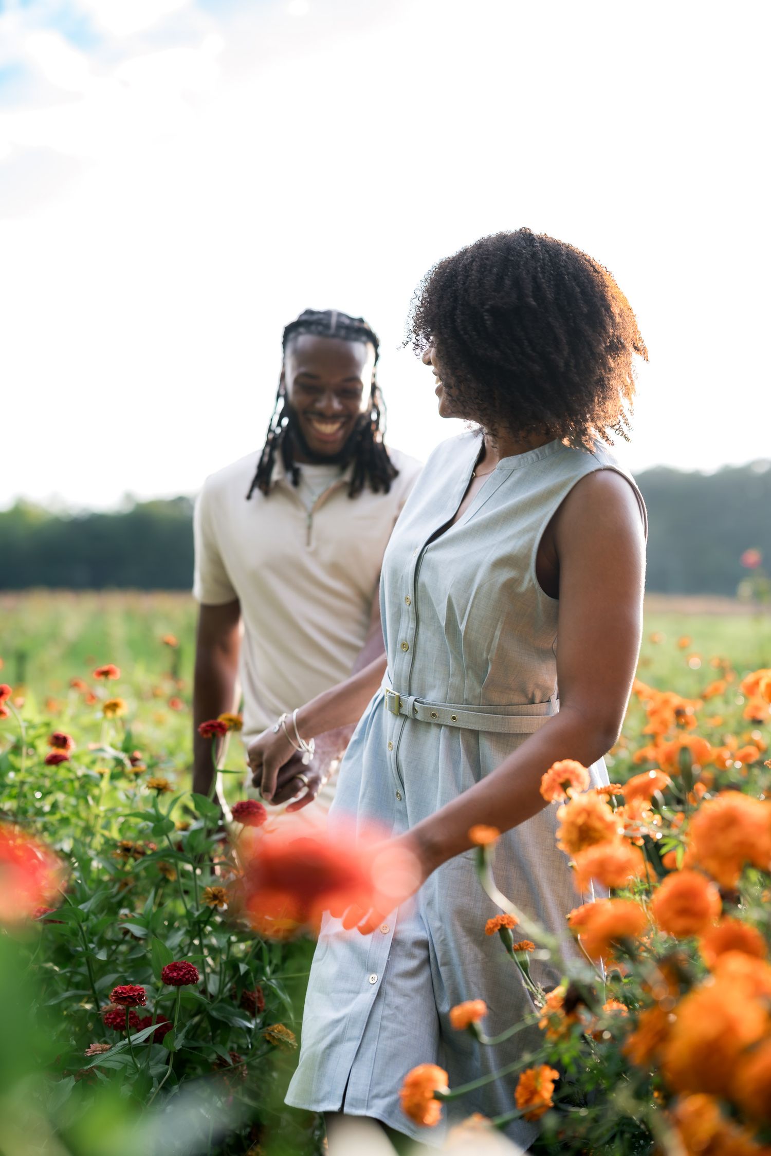 Couple smiling and picking colorful orange and red flowers together in a sunny blooming field.