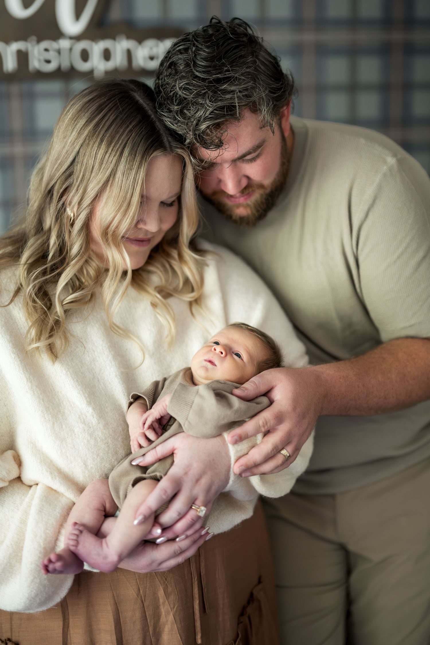 New parents tenderly hold their swaddled newborn baby together in a warm, intimate family portrait session.