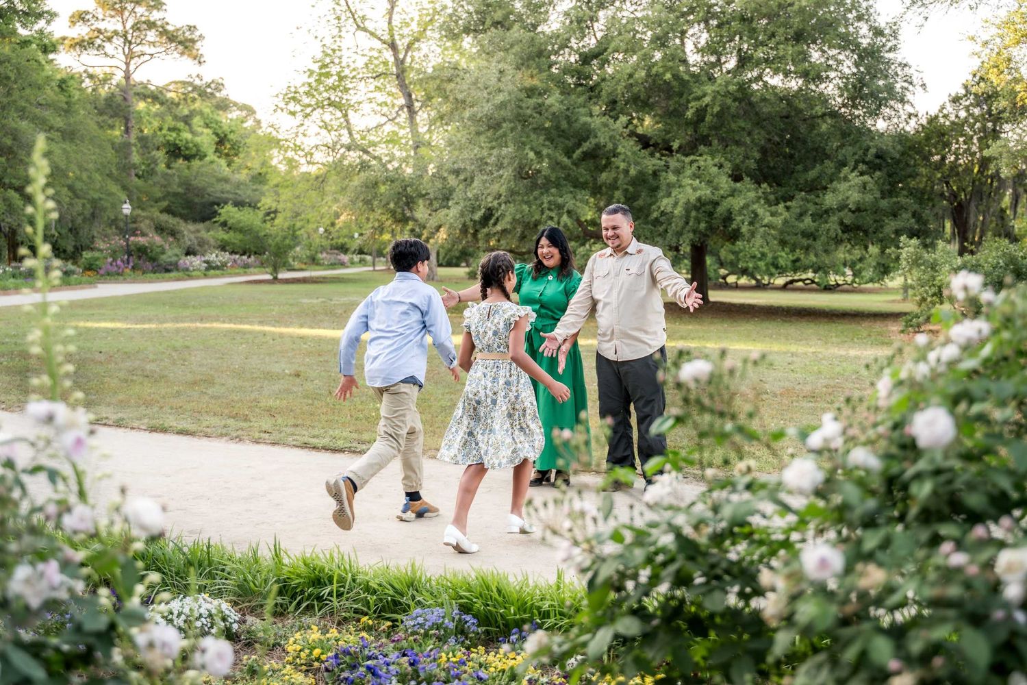 Hampton Park. A joyful family walks together on a garden path surrounded by lush greenery and blooming flowers.