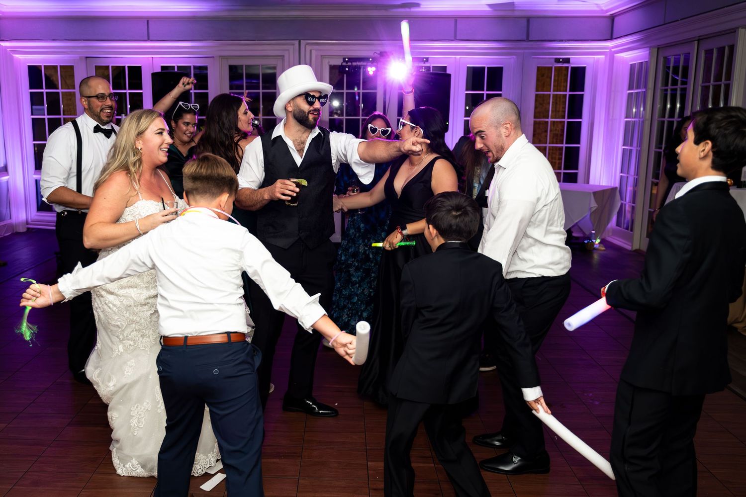 Dunes West Golf and River Club. Energetic wedding reception dance floor with guests dancing under purple lights holding glow sticks.