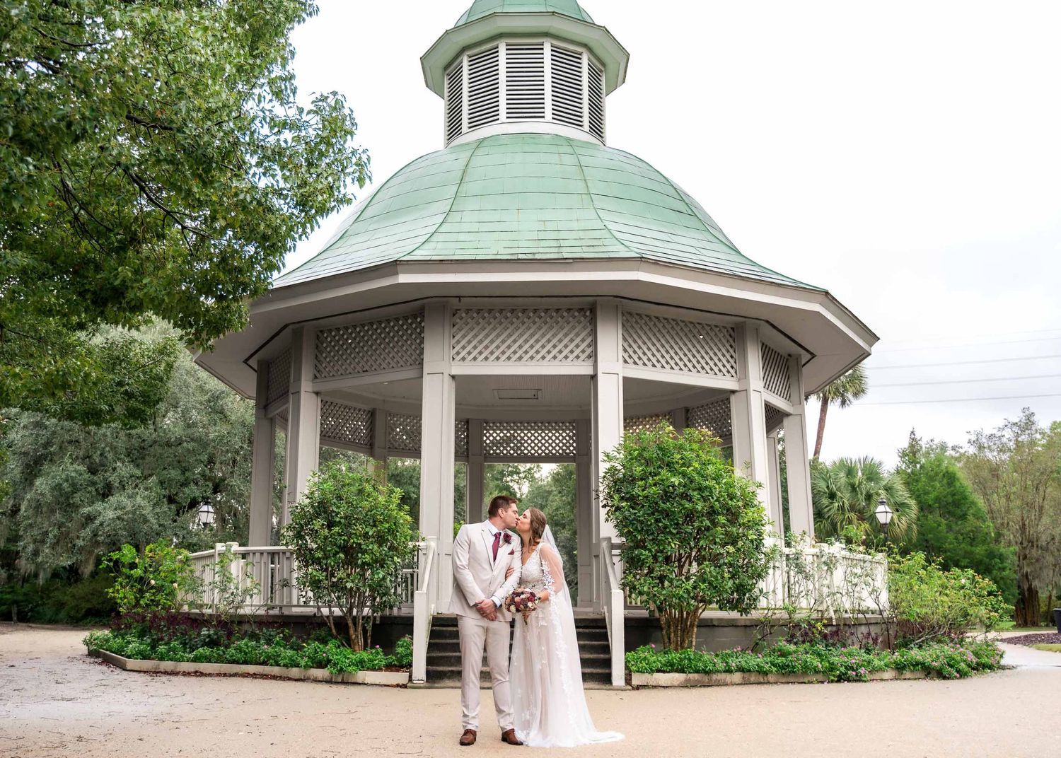 Hampton Park. Wedding couple sharing a kiss in front of an elegant white gazebo with green copper dome roof.