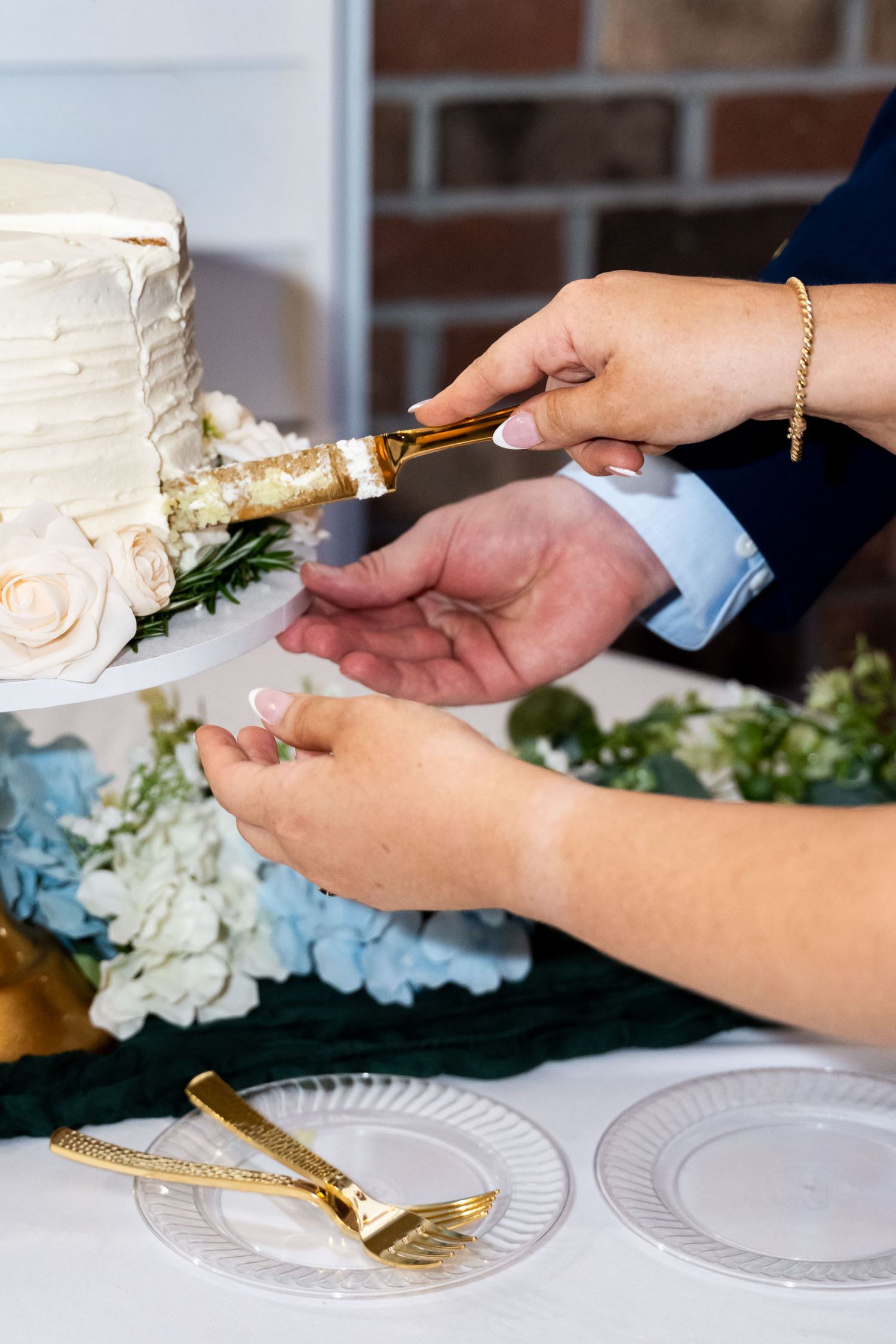 Bride and groom cutting white wedding cake with gold knife, blue hydrangeas and roses decorating the table.