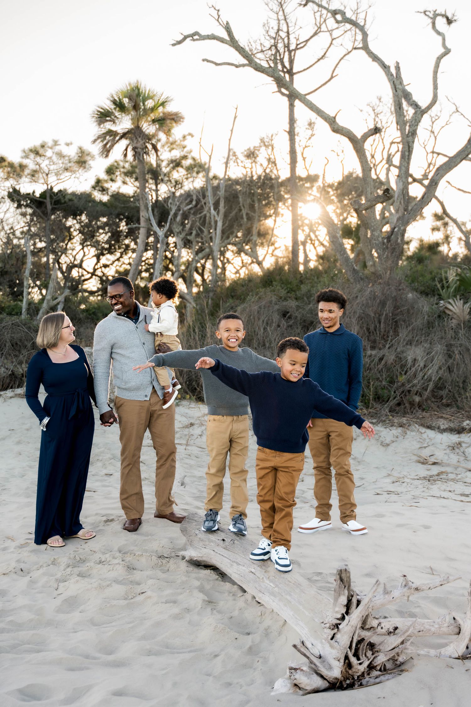 Folly Beach. Family of seven posing on sandy beach at sunset with driftwood and palm trees.