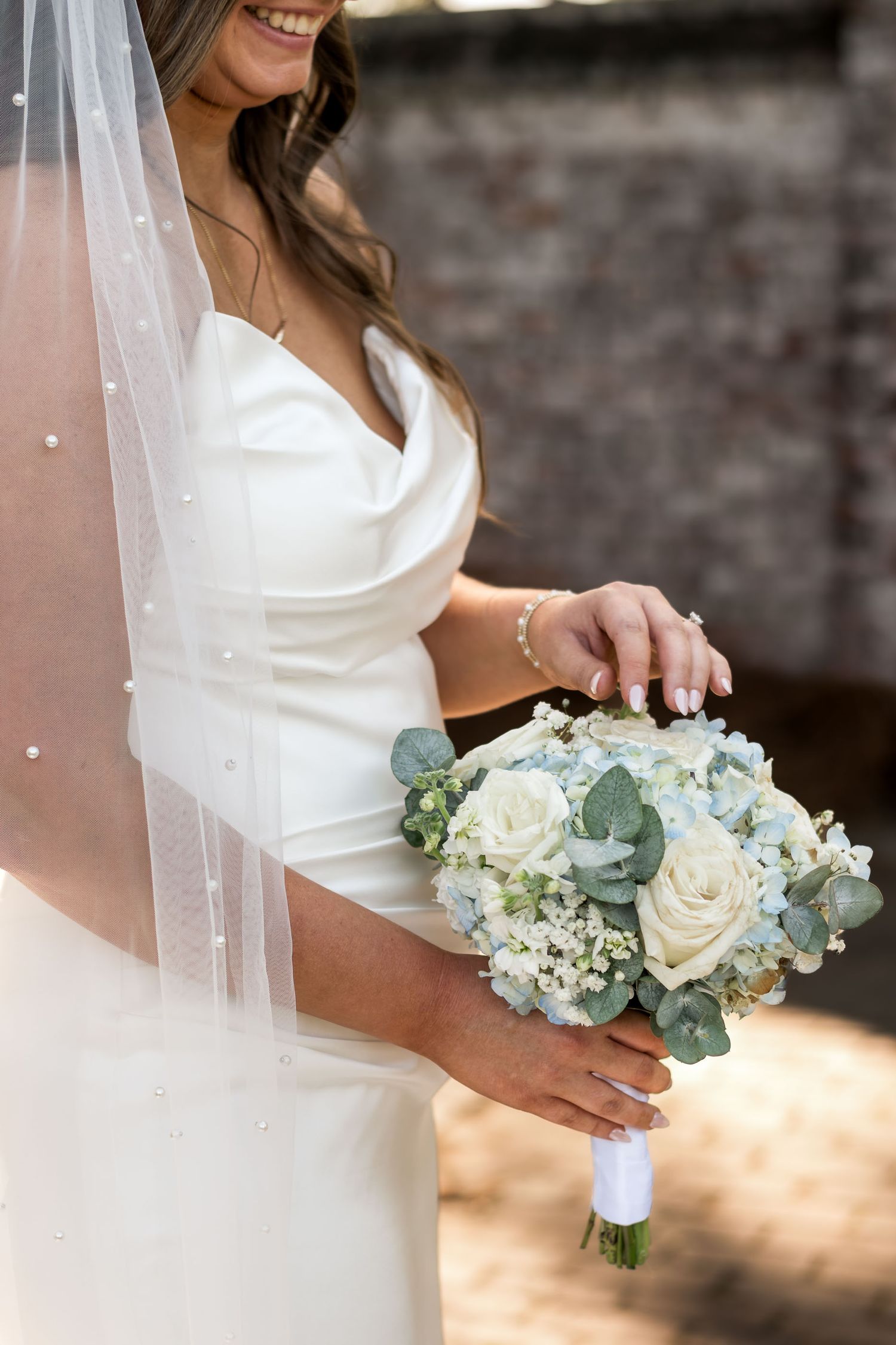 Dunes West Golf and River CBride in strapless white gown holding elegant bouquet of white roses, hydrangeas, and eucalyptus with pearl veil.