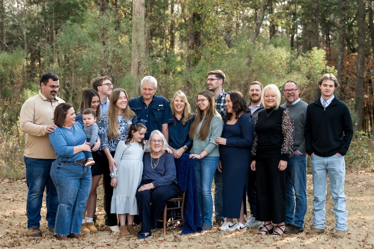 Large extended family group portrait outdoors in a pine forest wearing coordinated blue outfits.
