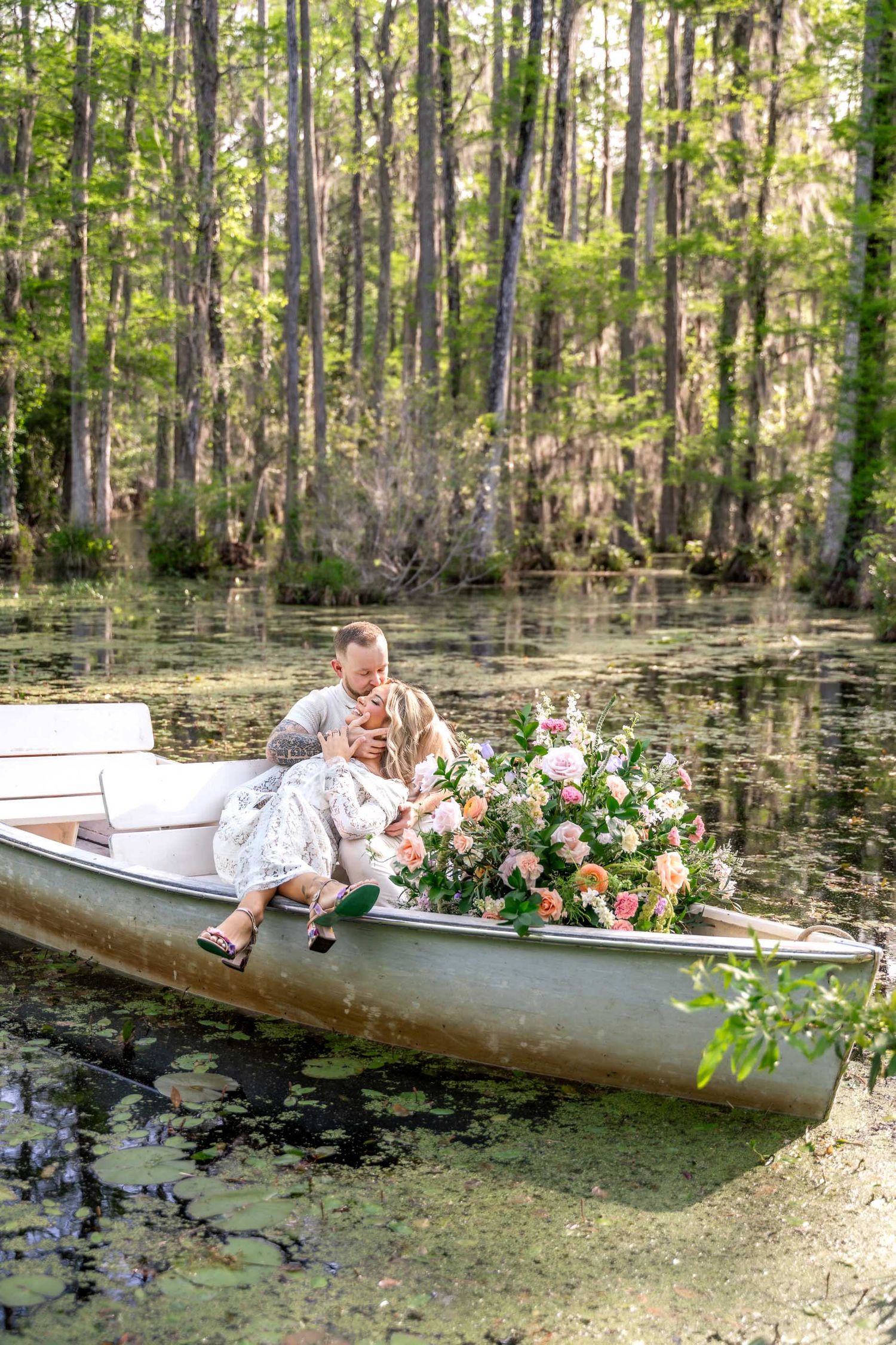 Cypress Gardens. Couple sharing a romantic kiss in a canoe adorned with lush pink florals on a serene cypress swamp.