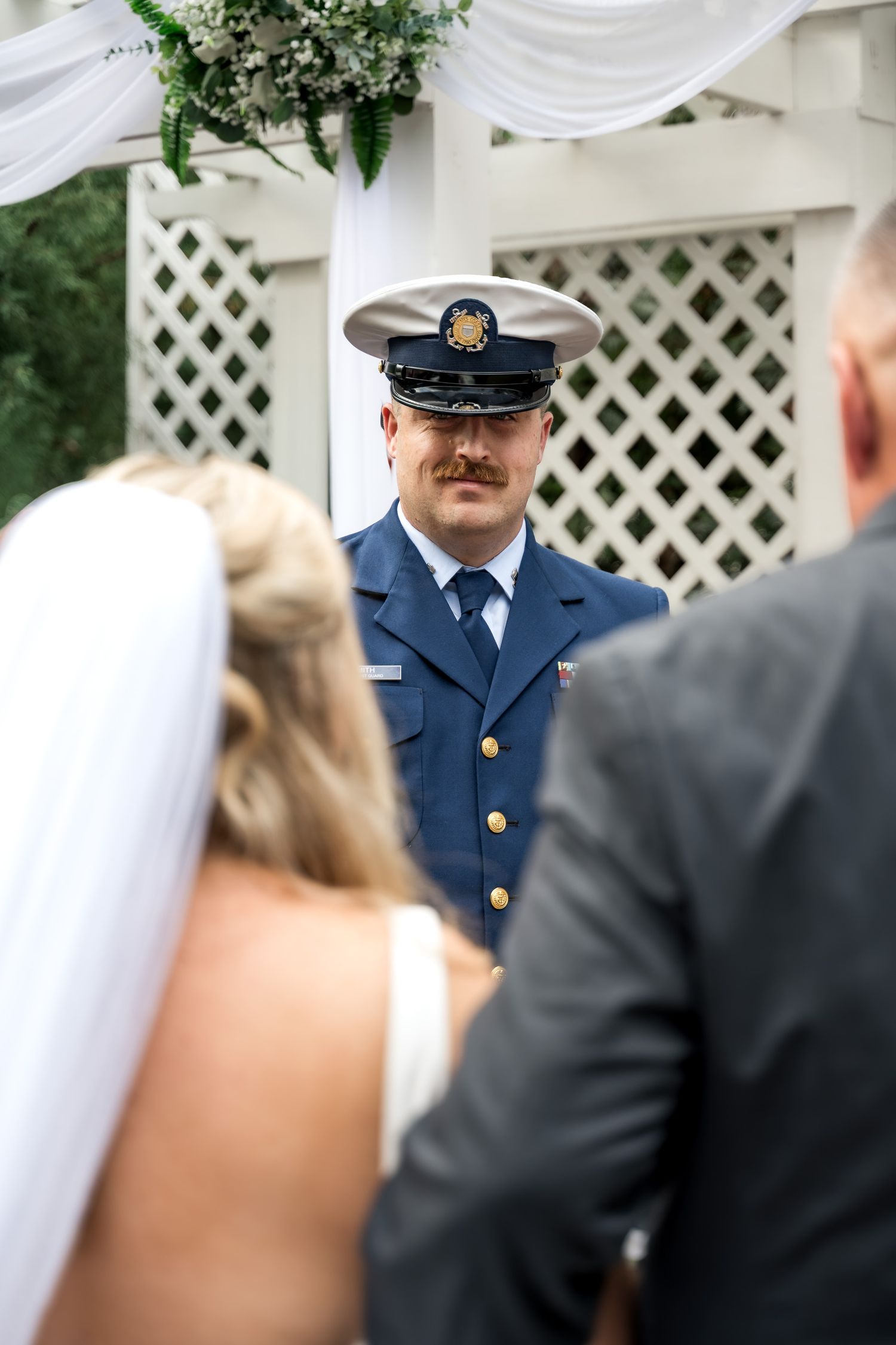 Coast Guard groom in dress uniform watching bride walk down aisle at outdoor wedding ceremony.
