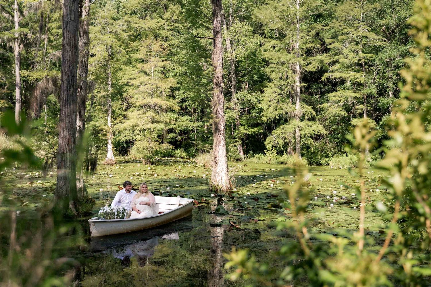 Couple enjoying a romantic boat ride through a lush, green cypress swamp with lily pads.