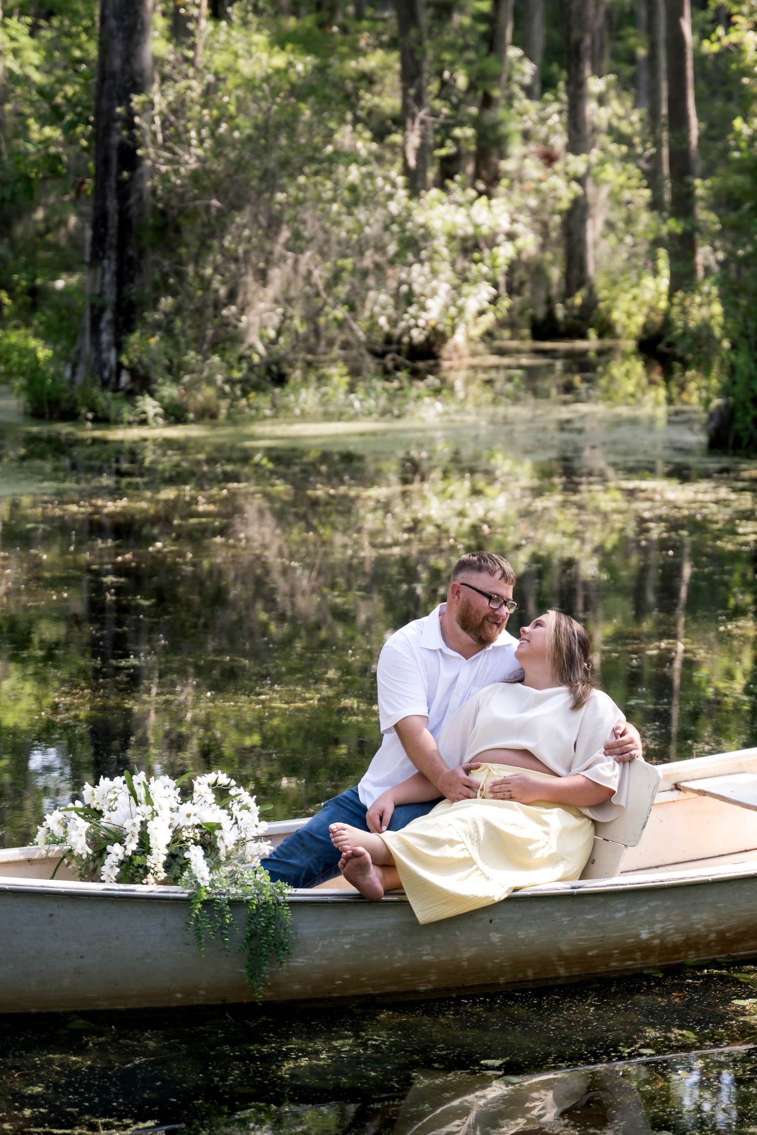 Couple sharing a romantic moment in a canoe surrounded by a lush, reflective swamp with white flowers in the bow.