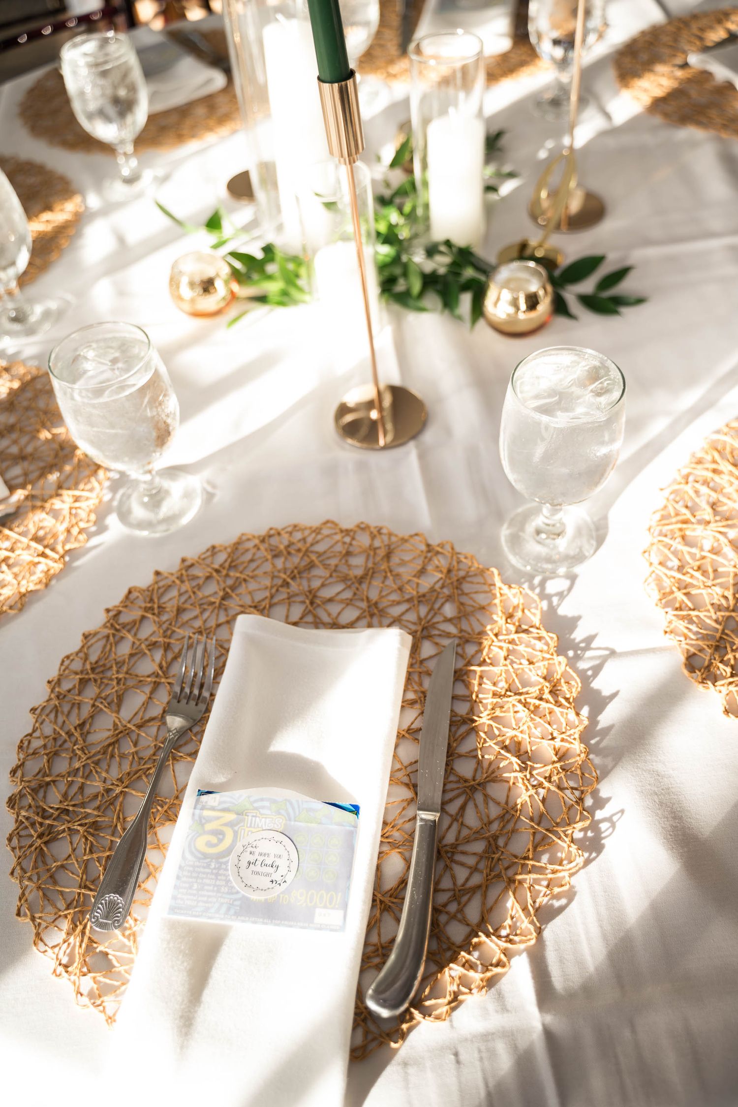 Dunes West Golf and River Elegant wedding table setting with woven gold charger plates, white napkins, crystal glassware, and green candles.