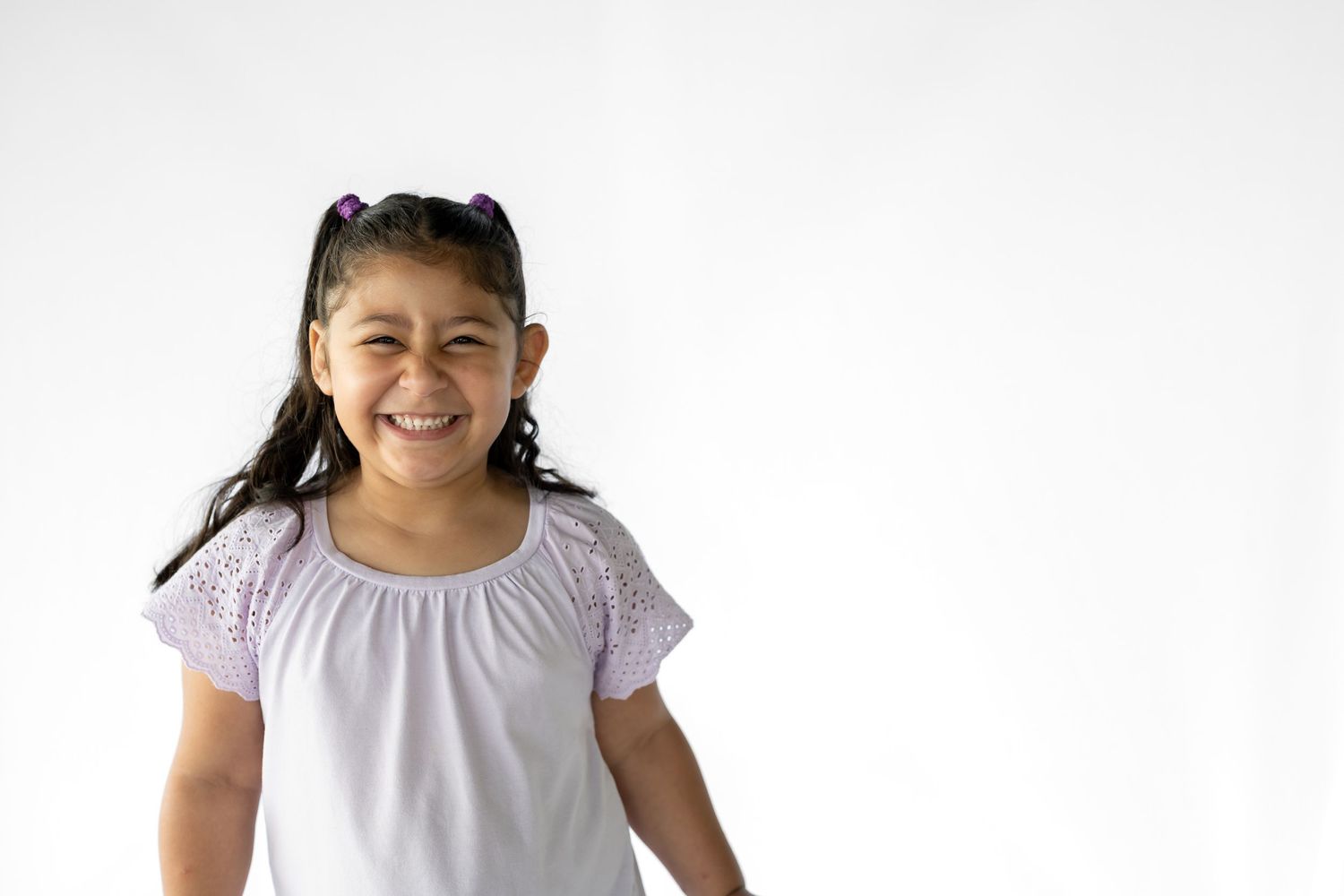 A happy young Latina girl with dark hair smiling brightly, wearing a white blouse on a white background.