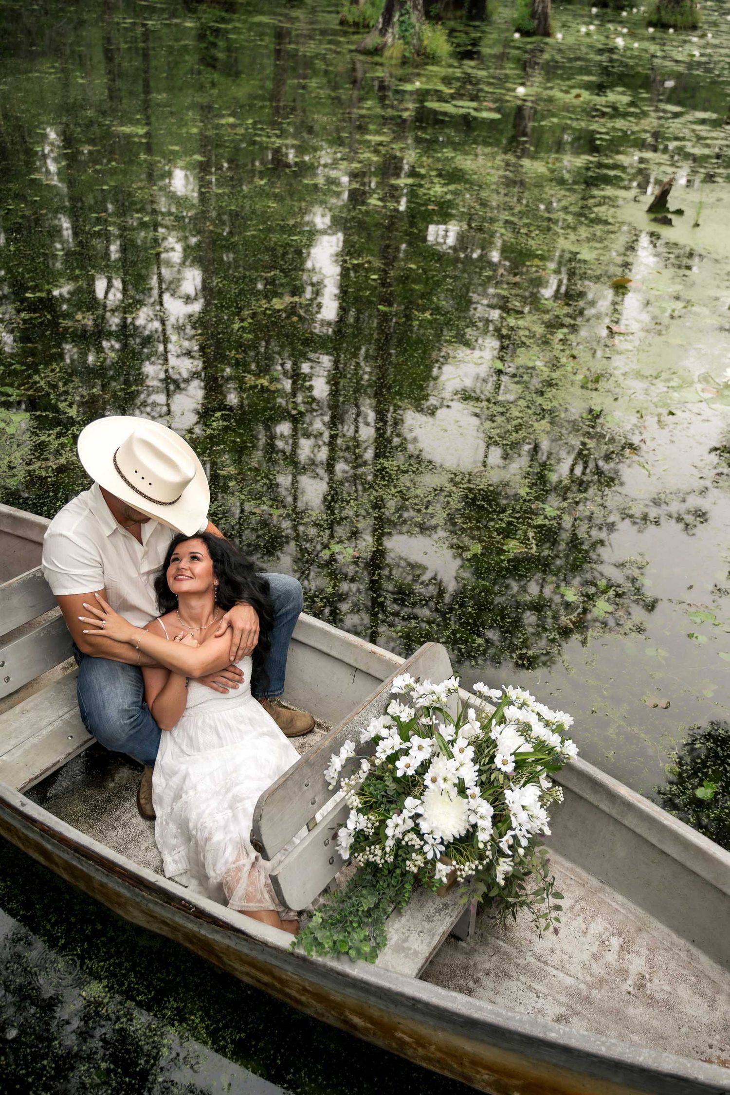 Cypress Gardens. Couple embraces romantically in a rustic boat surrounded by white flowers on a lush green pond.