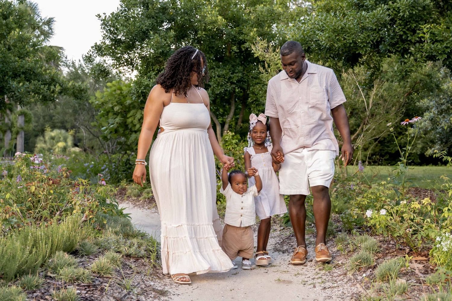 Hampton Park. Happy family of four strolls along a garden path surrounded by colorful flowers and lush greenery.