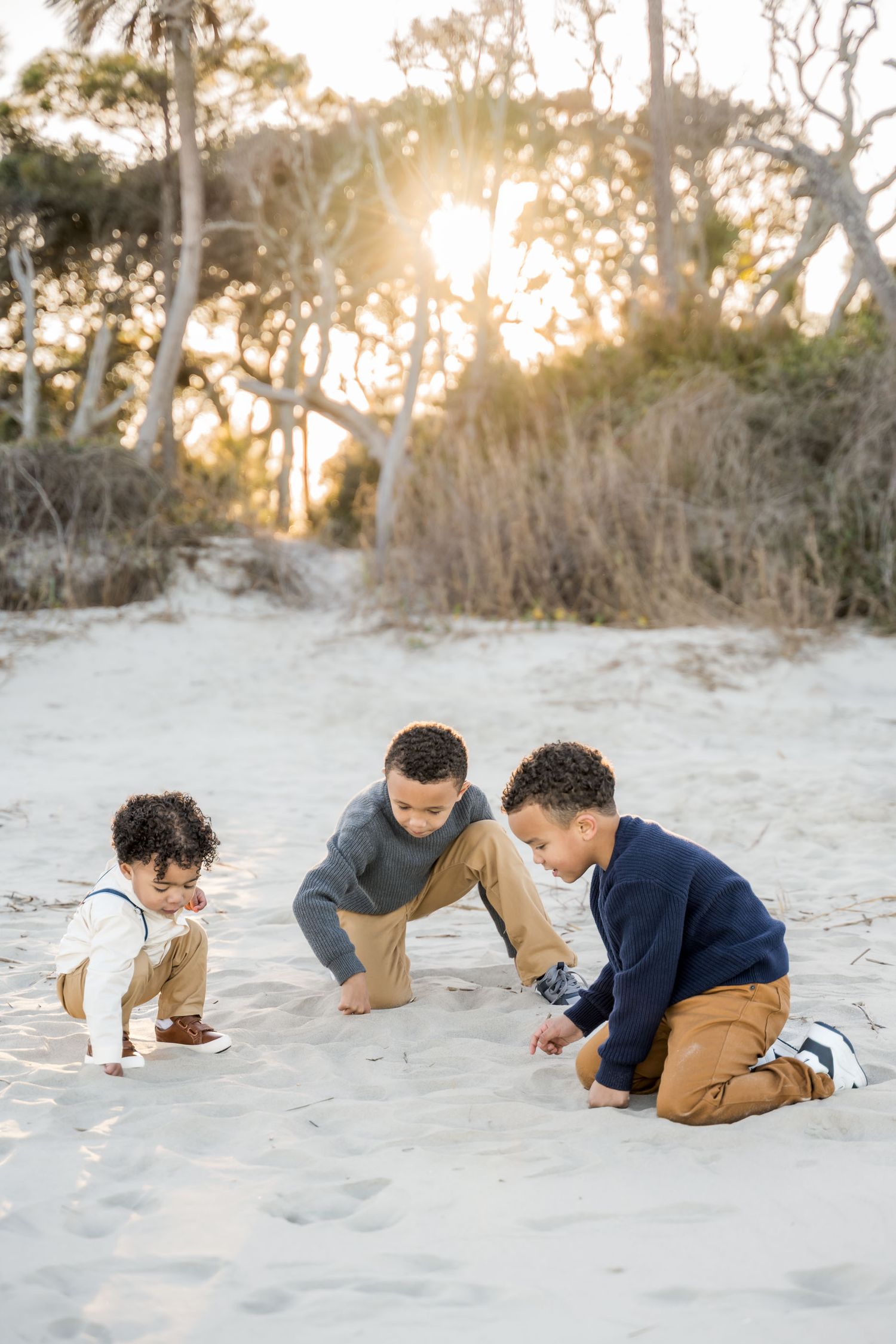 Folly Beach. Three young boys playing in the sand at golden hour on a beach, surrounded by trees with sunlight streaming through.