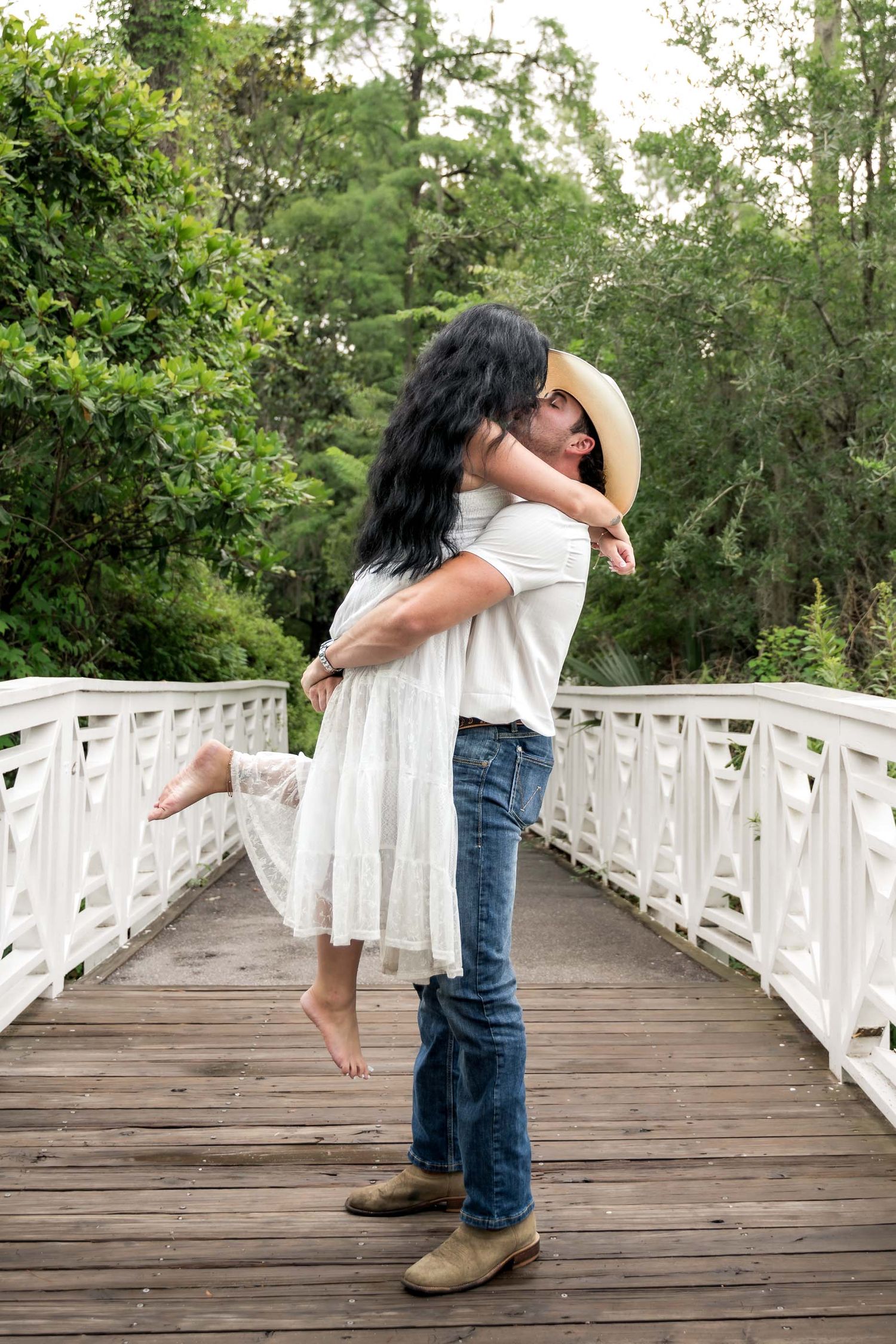 Man lifting woman in a joyful embrace on a white wooden bridge outdoors.