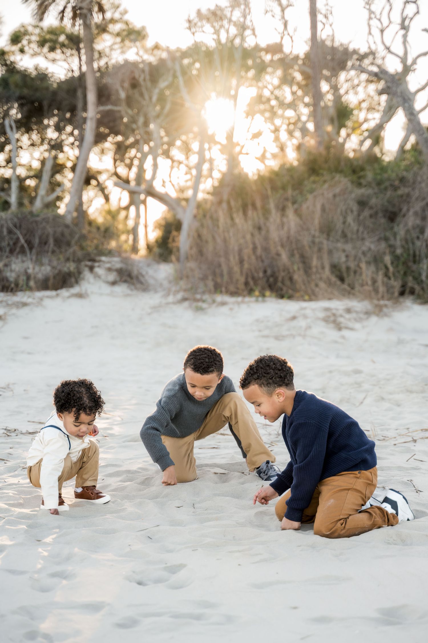 Folly Beach. Three young brothers playing together in the sand on a beach at golden hour.