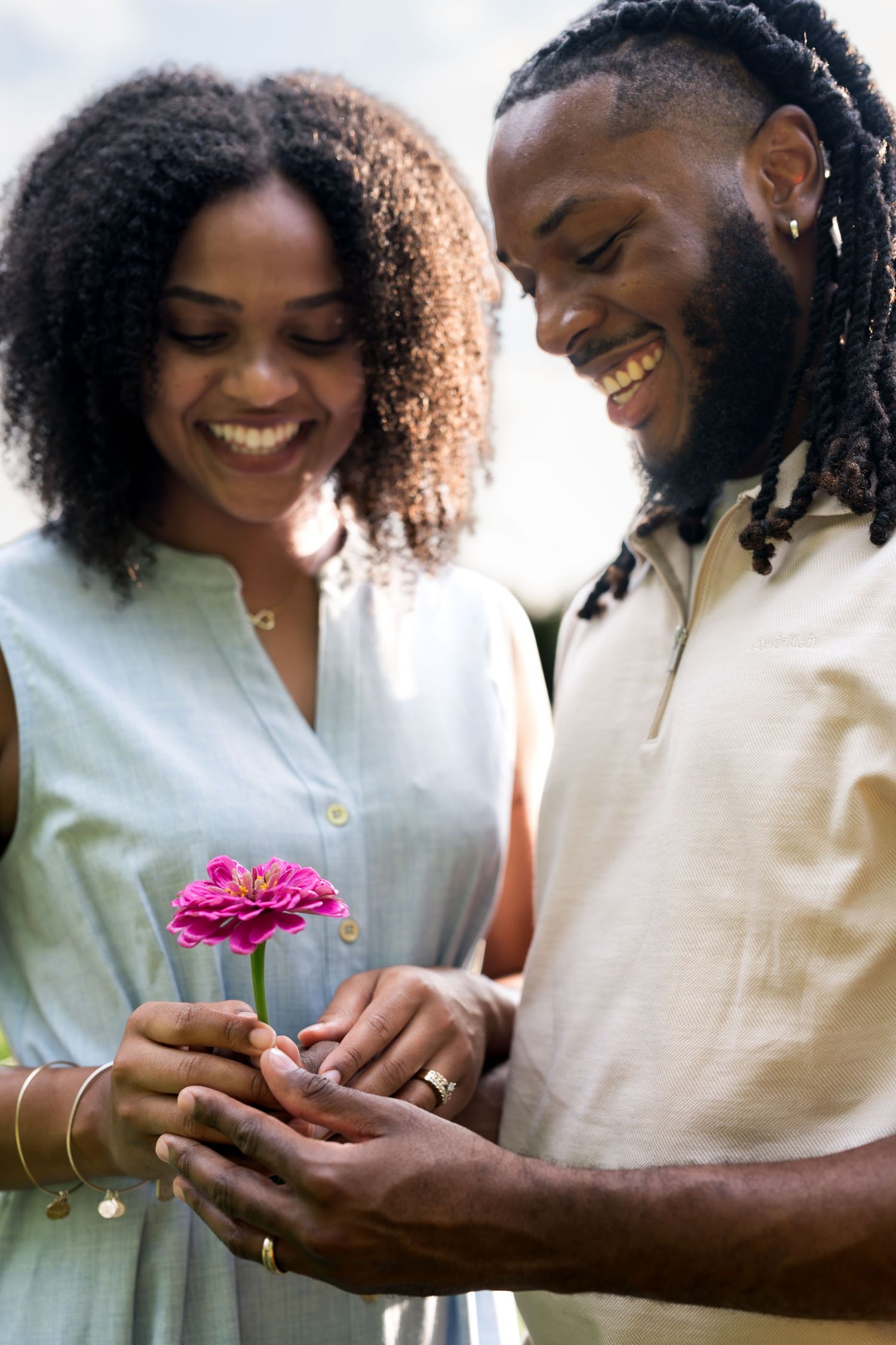 A smiling Black couple shares a tender moment as the man gives the woman a pink zinnia flower outdoors.