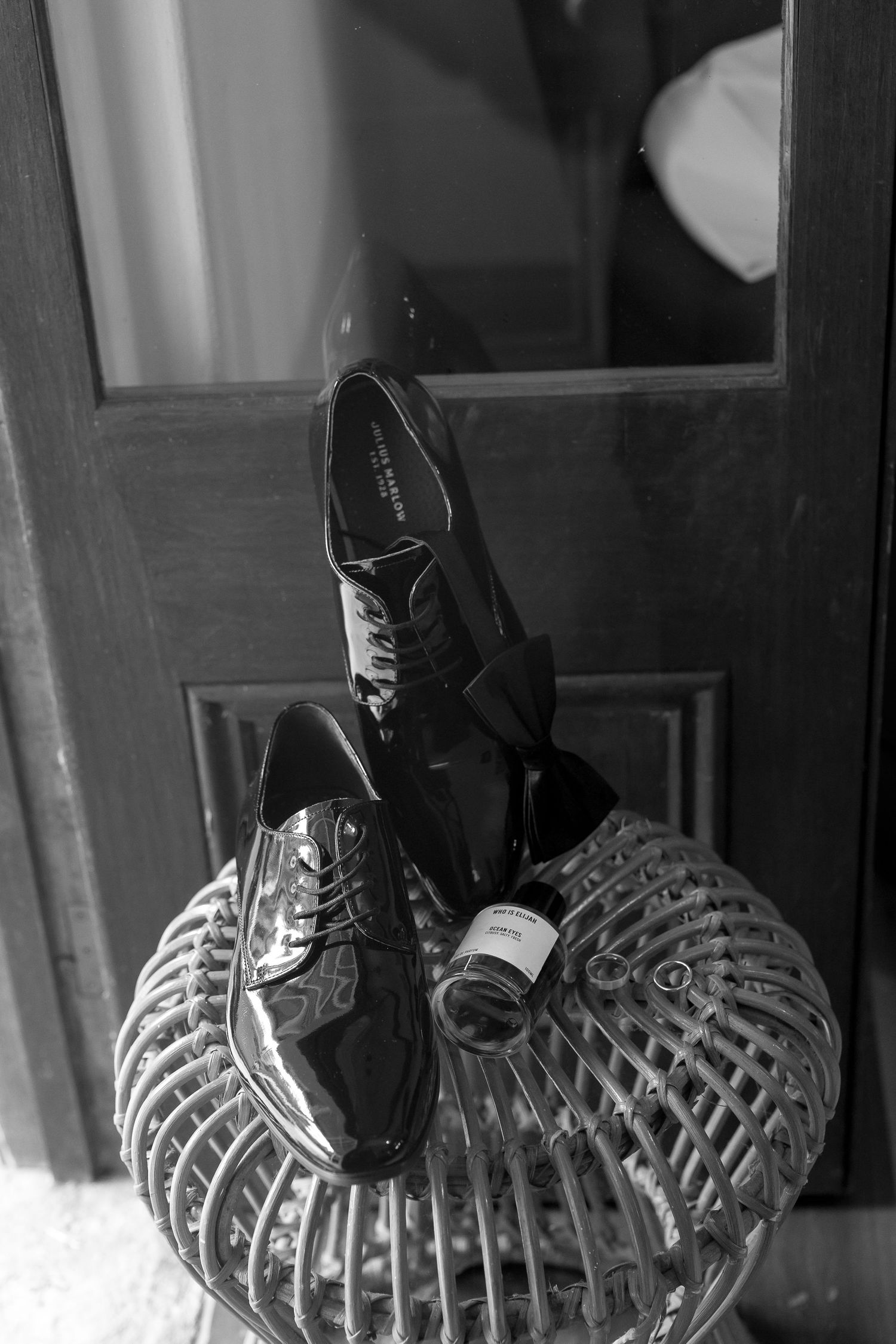 Black and white photo of polished dress shoes on a wicker stand near a door.