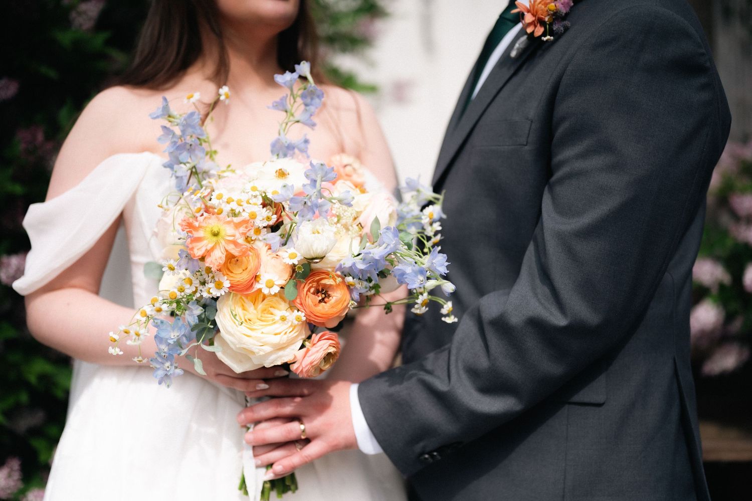 Beautiful wedding bouquet with peach and lavender flowers held between couple in formal wedding attire.