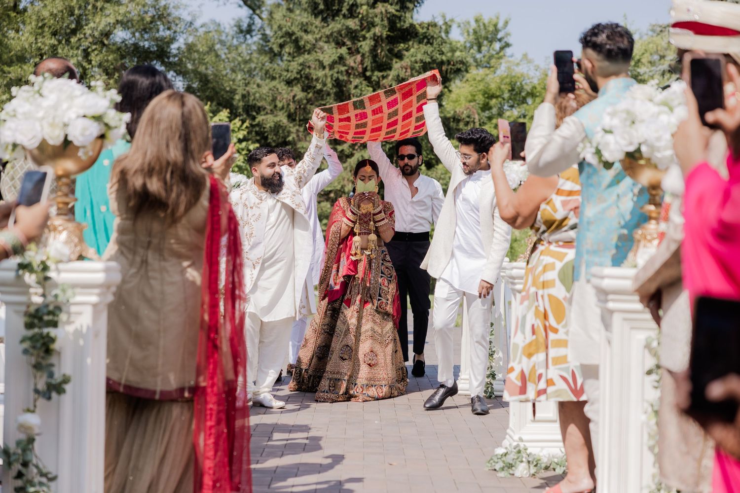 Wedding guests line up outdoors on stone steps for a celebratory group photo on a sunny day.