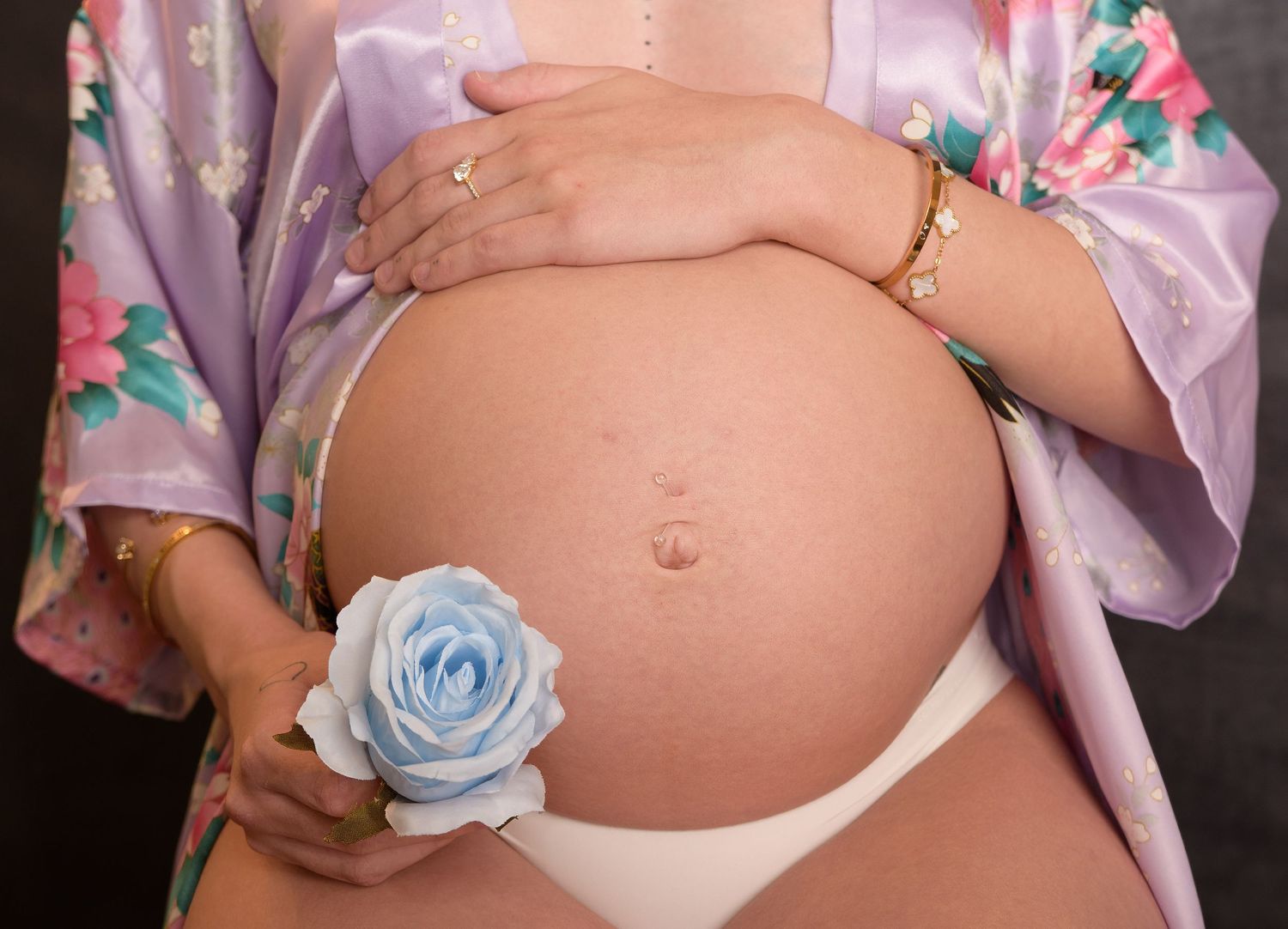 A pregnant woman's belly is shown in a pink floral robe with a blue rose accent.