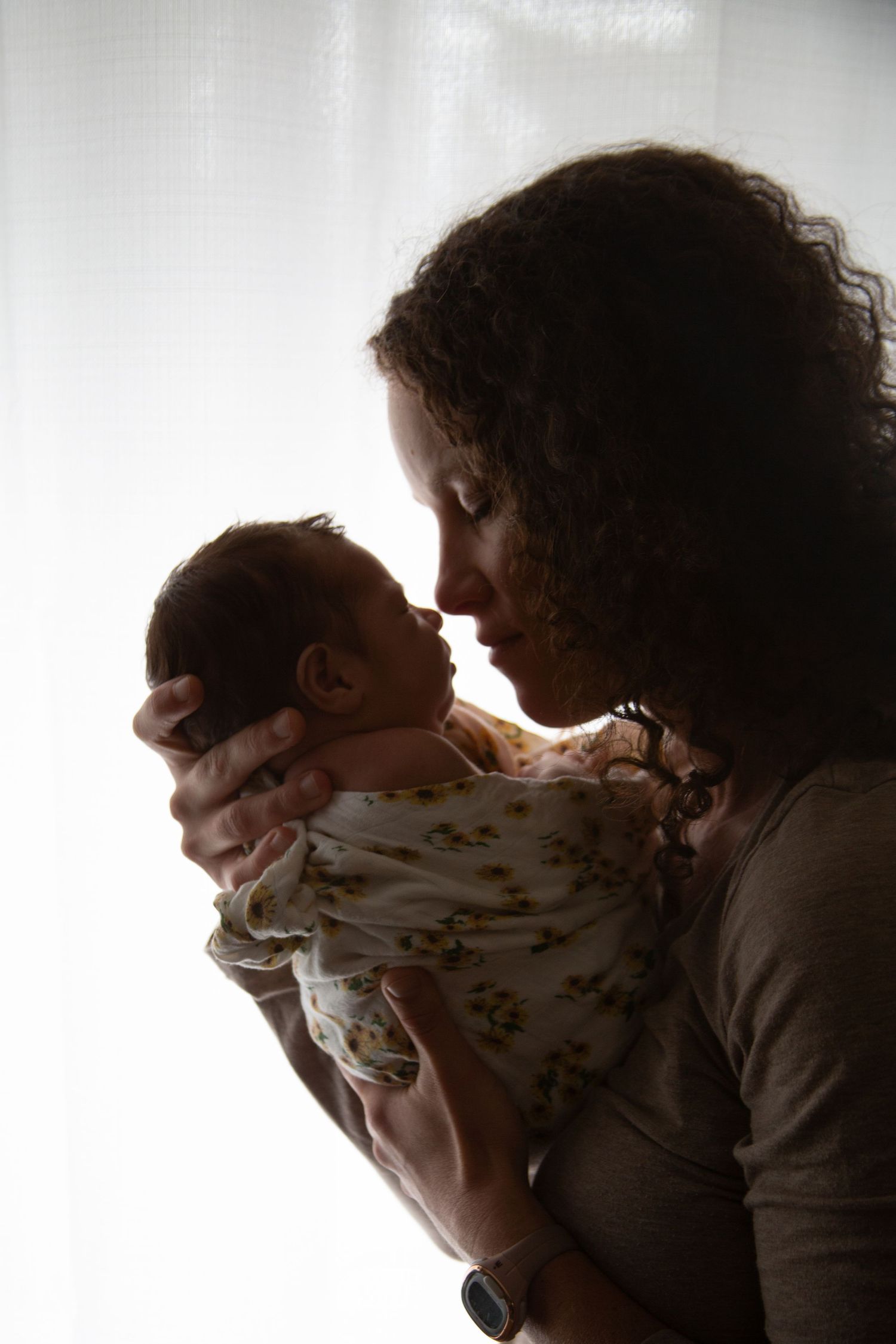 Silhouette profile of tender moment with baby against bright window.