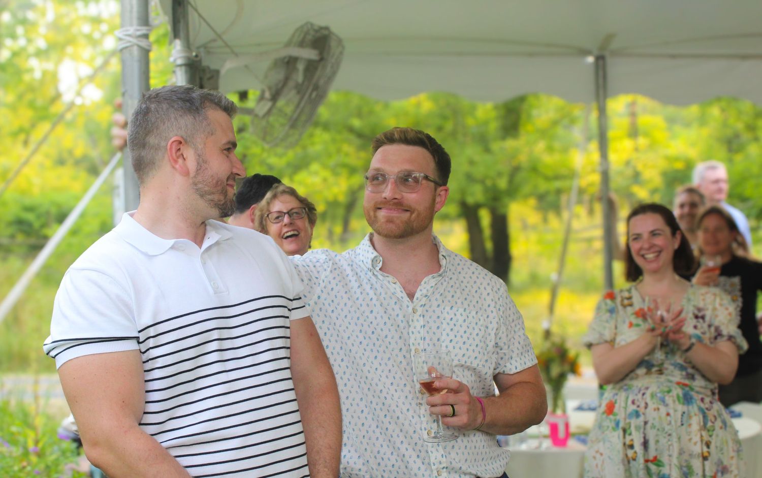 Guests mingling and laughing at an outdoor celebration under a white tent.
